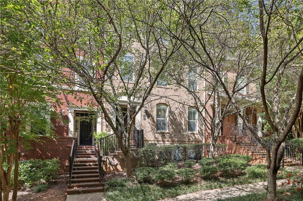 Brick townhouse frontage with multiple stairways and entrances beneath mature trees.