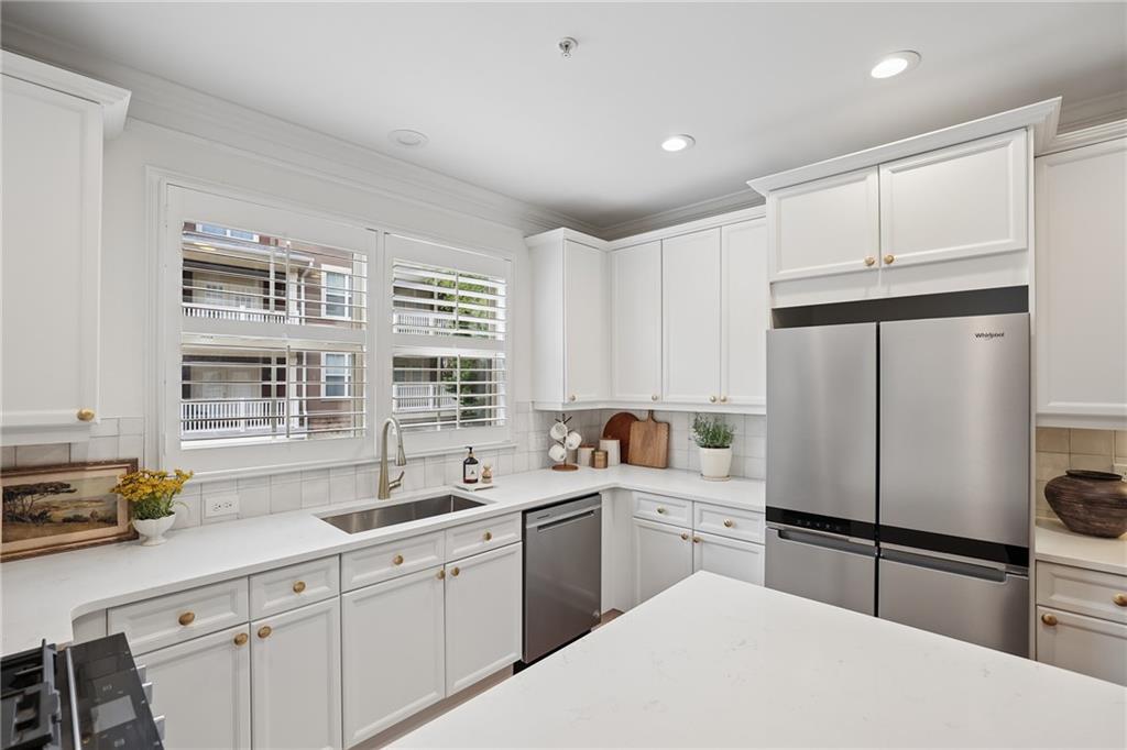 Bright white kitchen with a large island, stainless steel appliances, and a window over the sink.