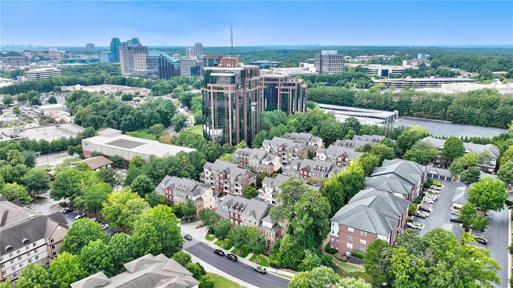 Aerial view of townhomes near a glass office tower and wooded skyline.