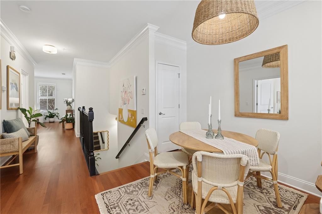Dining area with a round wooden table, woven chairs, and a patterned rug beside a hardwood hallway.