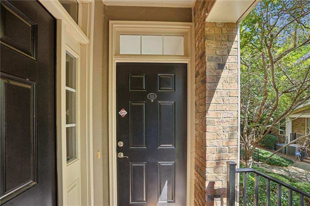 Covered home entry with a black paneled door marked 521, brick column, and porch railing.