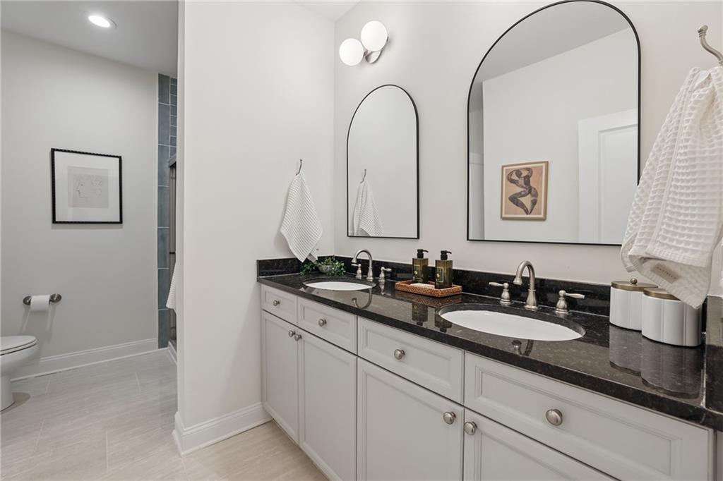 Bathroom with a double-sink vanity, dark countertop, and arched mirrors.