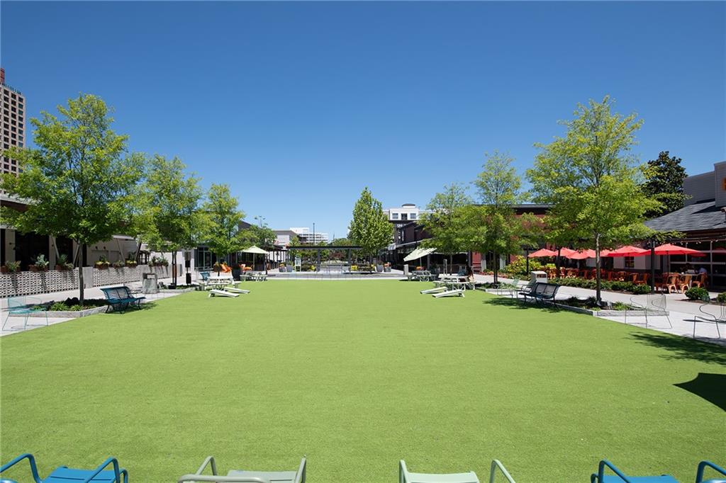 Outdoor courtyard with a wide green lawn, lounge chairs, and restaurants with red umbrellas.