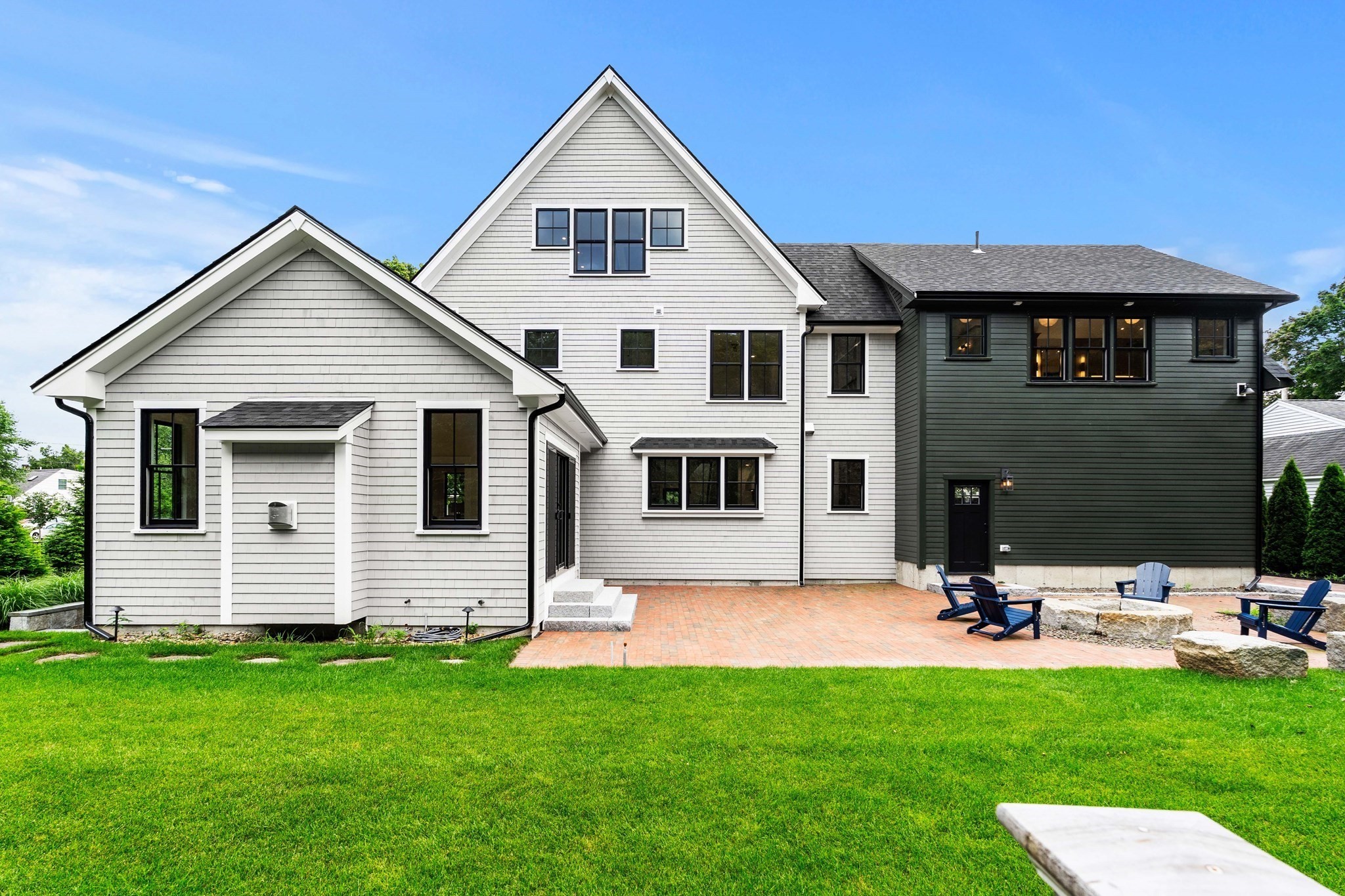 Rear of a two-story white and dark green house with a brick patio and Adirondack chairs.