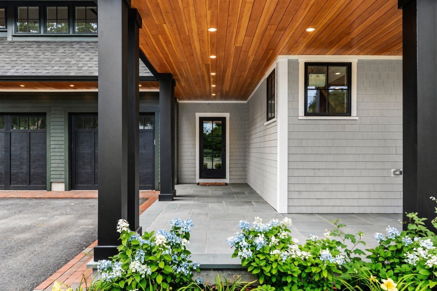 Modern home’s covered entry with a wood ceiling, stone paving, and flowering hydrangeas.