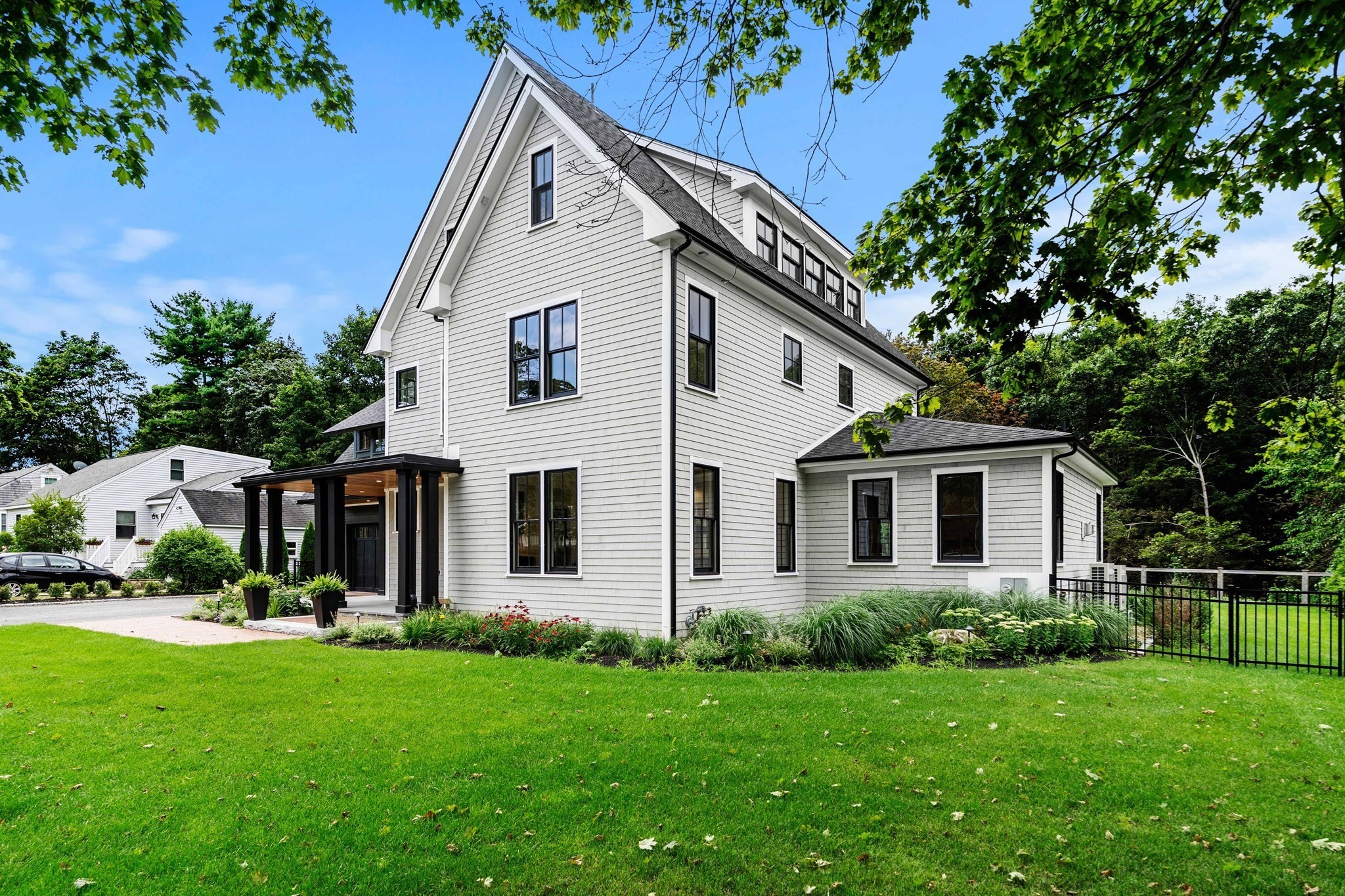 White clapboard house with a steep gabled roof, covered entry, landscaped garden beds, and green lawn.