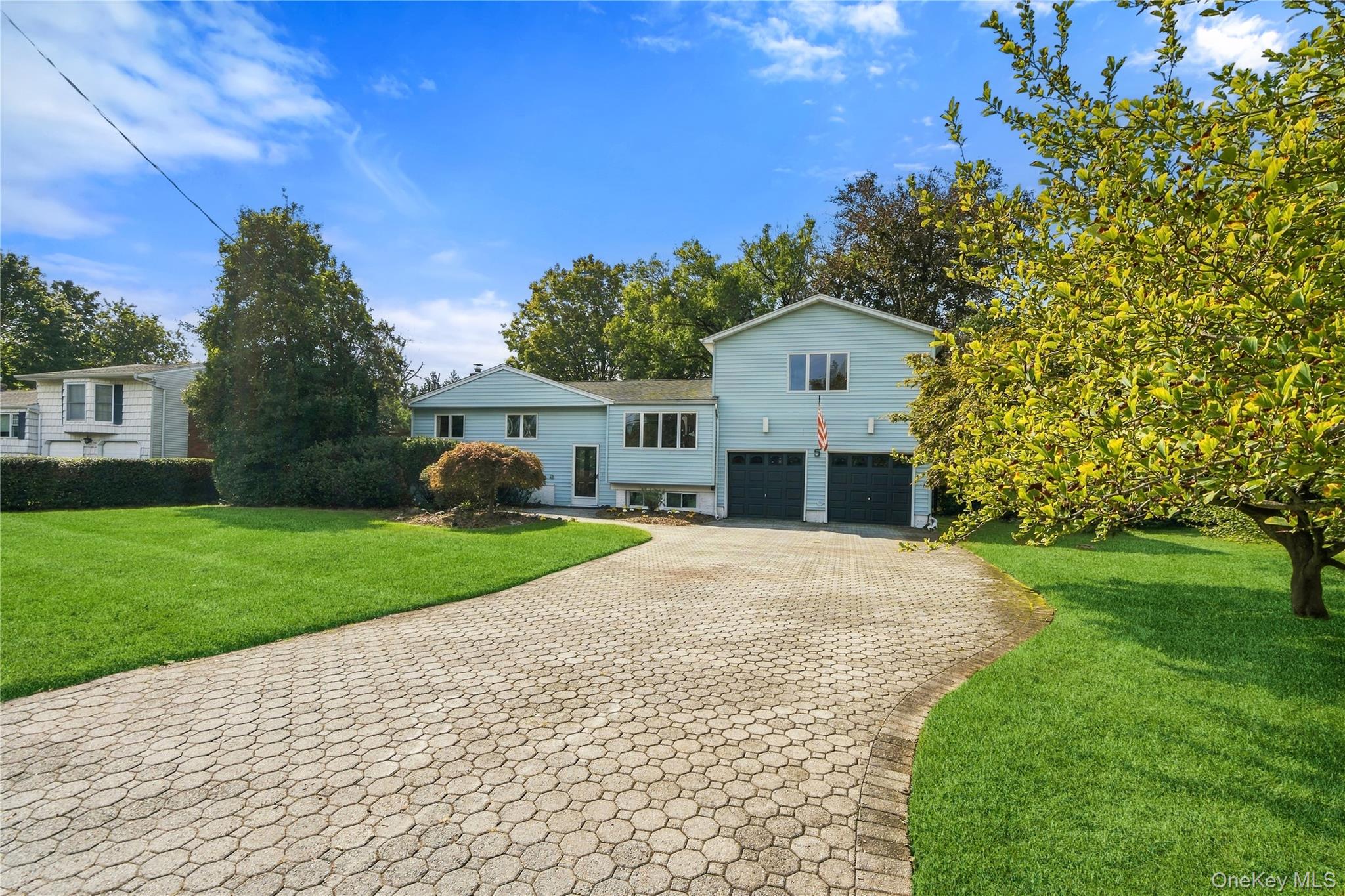 Light blue split-level home with two garage doors and a curved paver driveway.