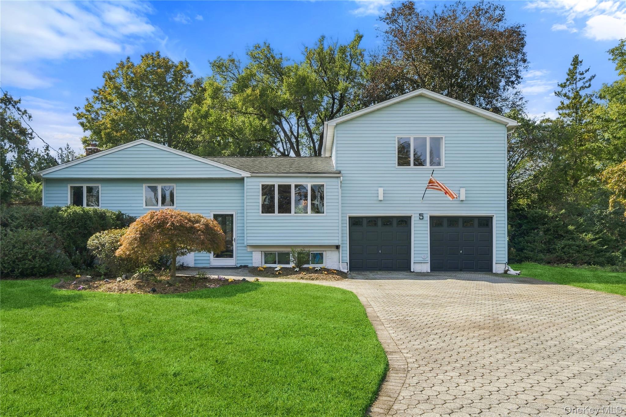 Light blue two-story home with two garage doors, a curved paver driveway, and a green lawn.