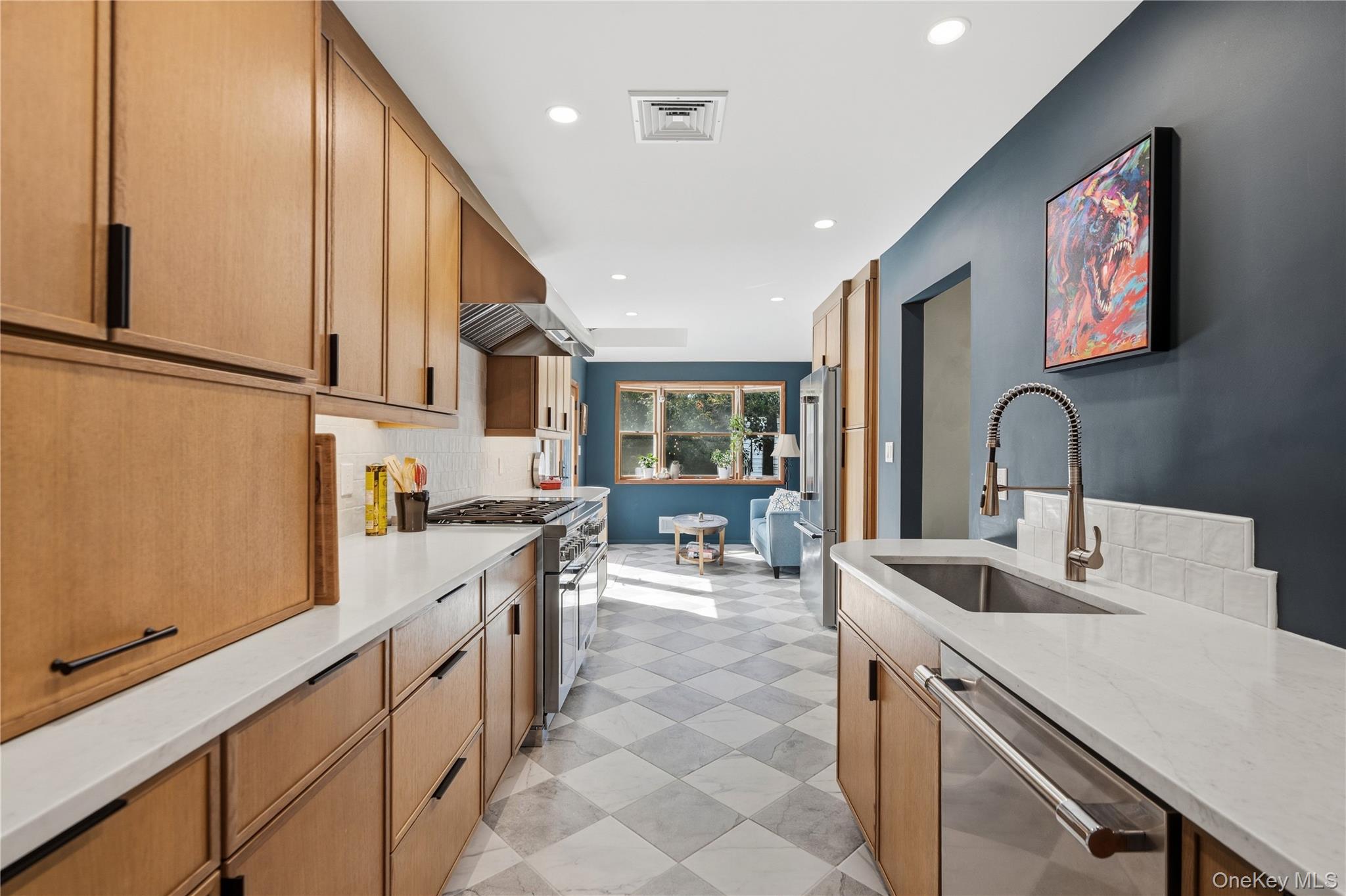 Long kitchen with wood cabinets, white counters, stainless steel appliances, and a sunny seating nook.