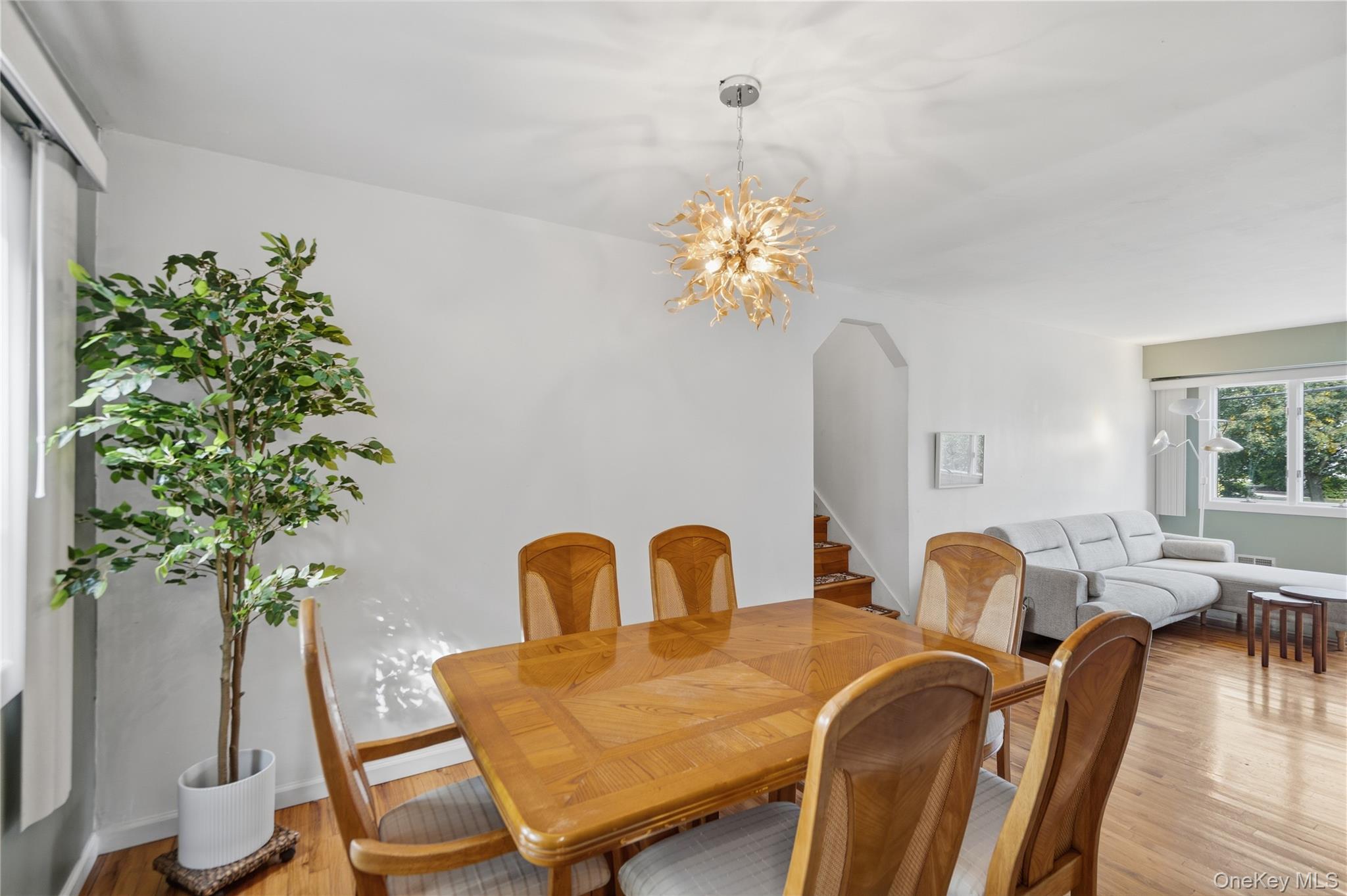Dining area with a wood table and sculptural pendant beside a living room with a gray sectional.