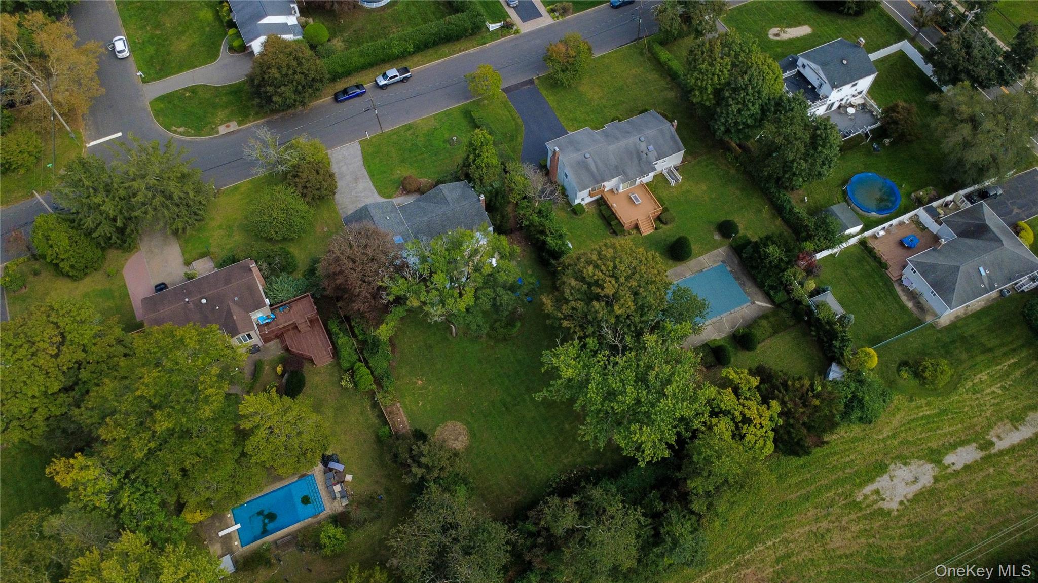 Aerial view of a house with a wooden deck and spacious lawn among leafy neighboring properties.