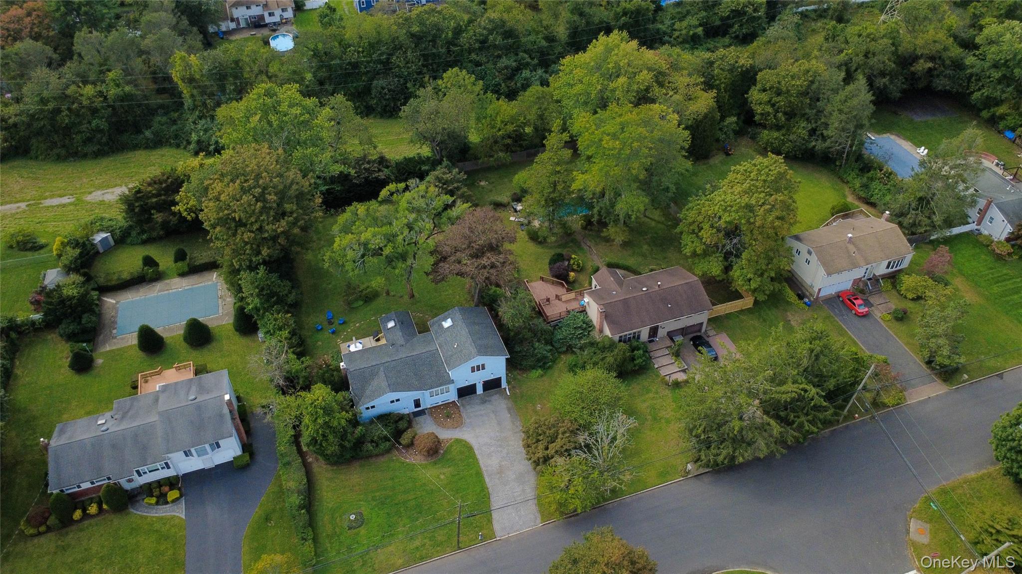 Aerial view of a residential property amid tree-lined yards, with neighboring homes and swimming pools.