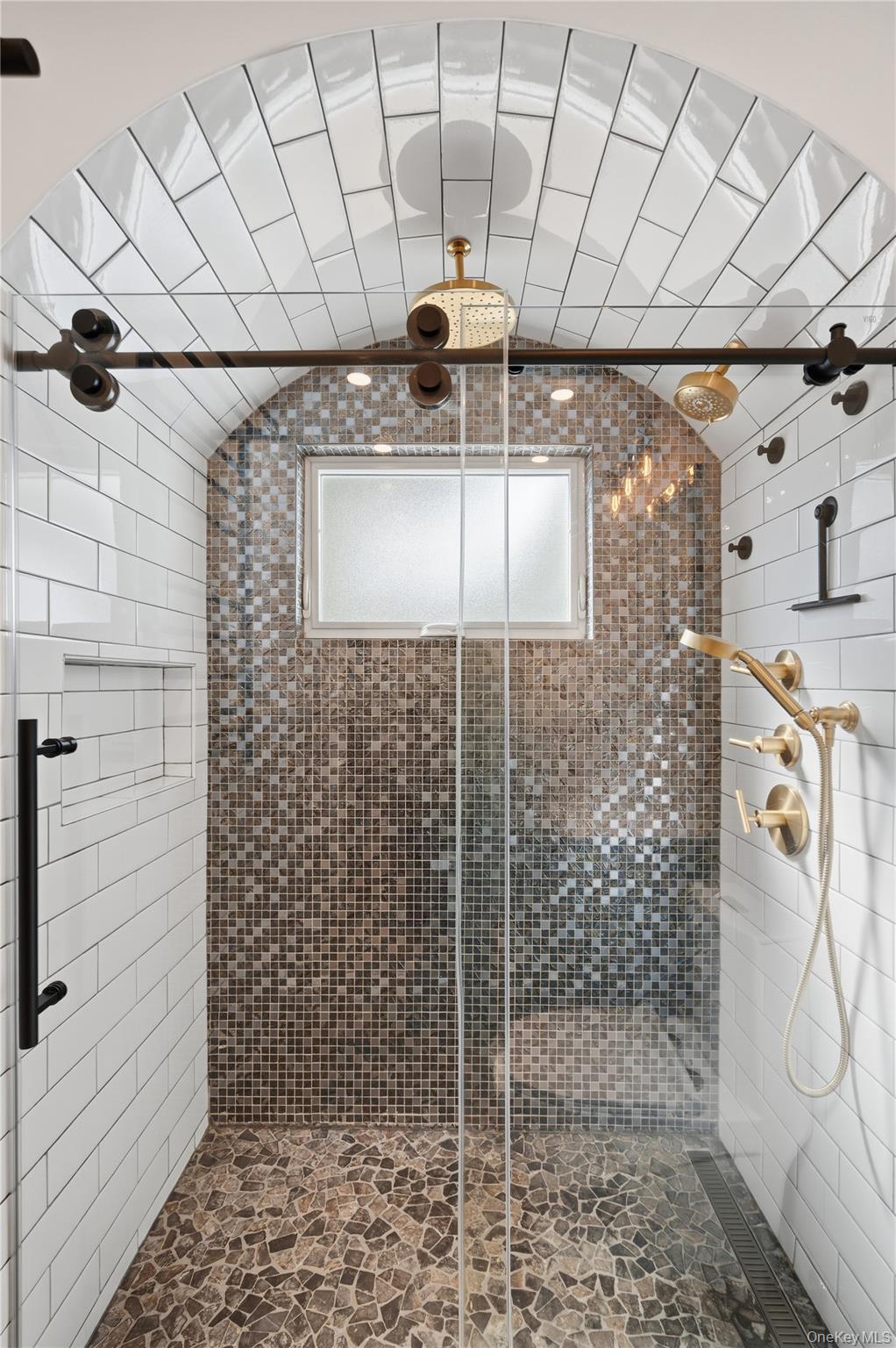 Walk-in shower with an arched tiled ceiling, mosaic walls, and brass fixtures.