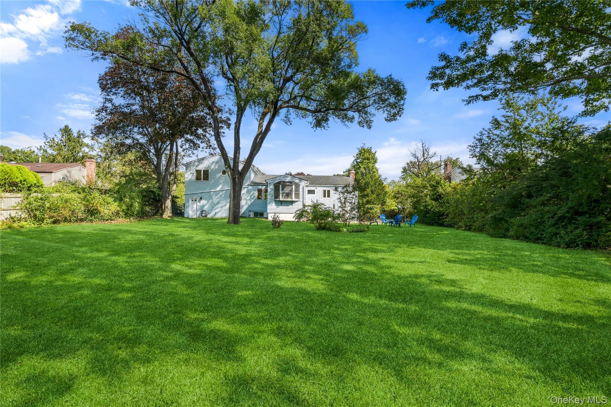 Rear of a light-colored house beyond a broad lawn shaded by mature trees.
