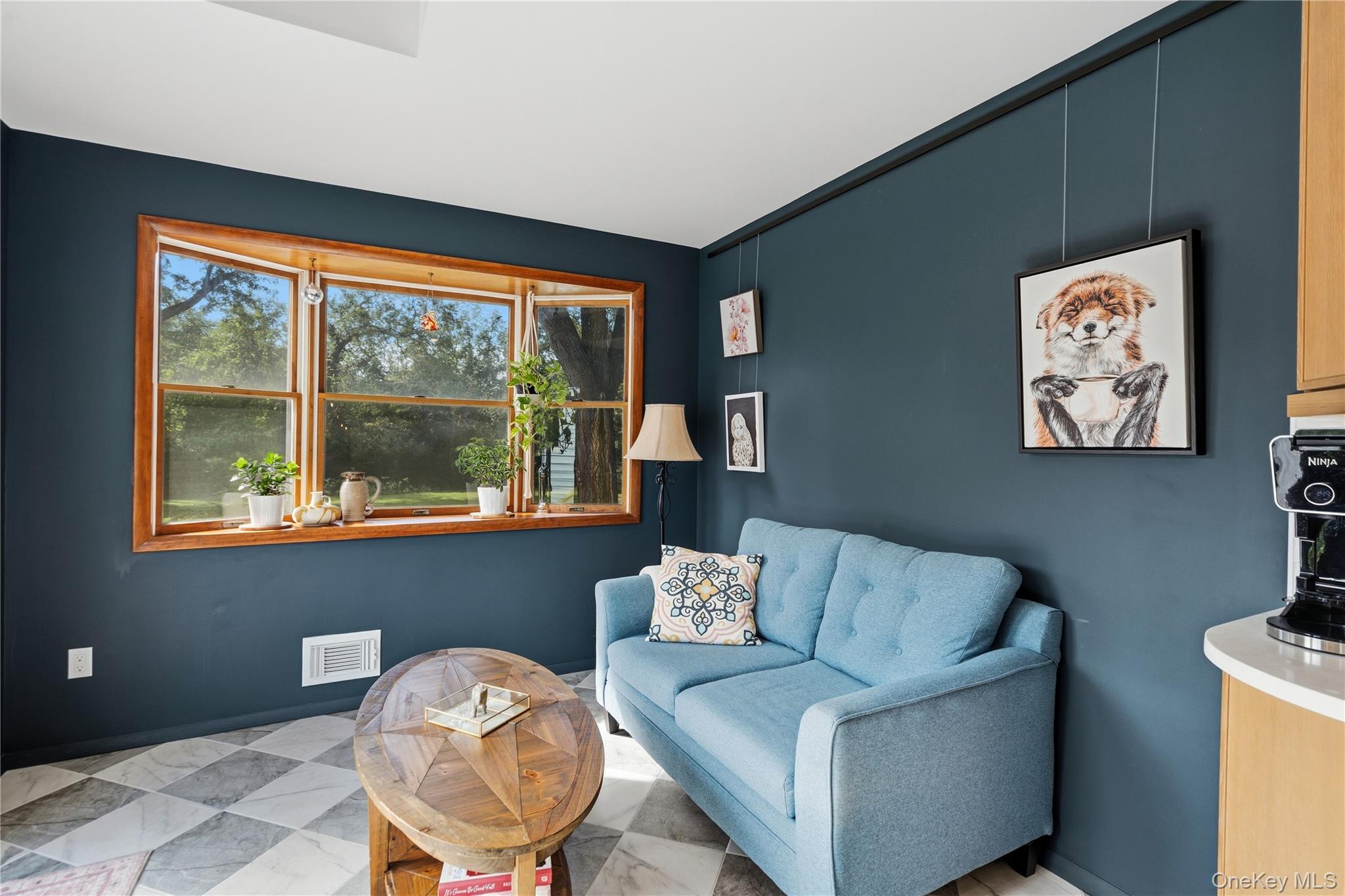 Sitting area with a blue sofa, round wooden coffee table, and wide window overlooking trees.
