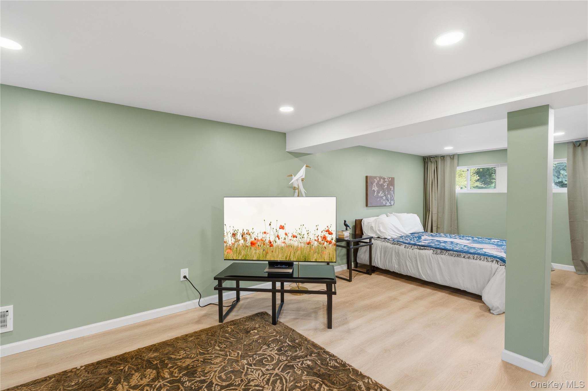 Bedroom with pale green walls, a bed by the window, and a television on a console.