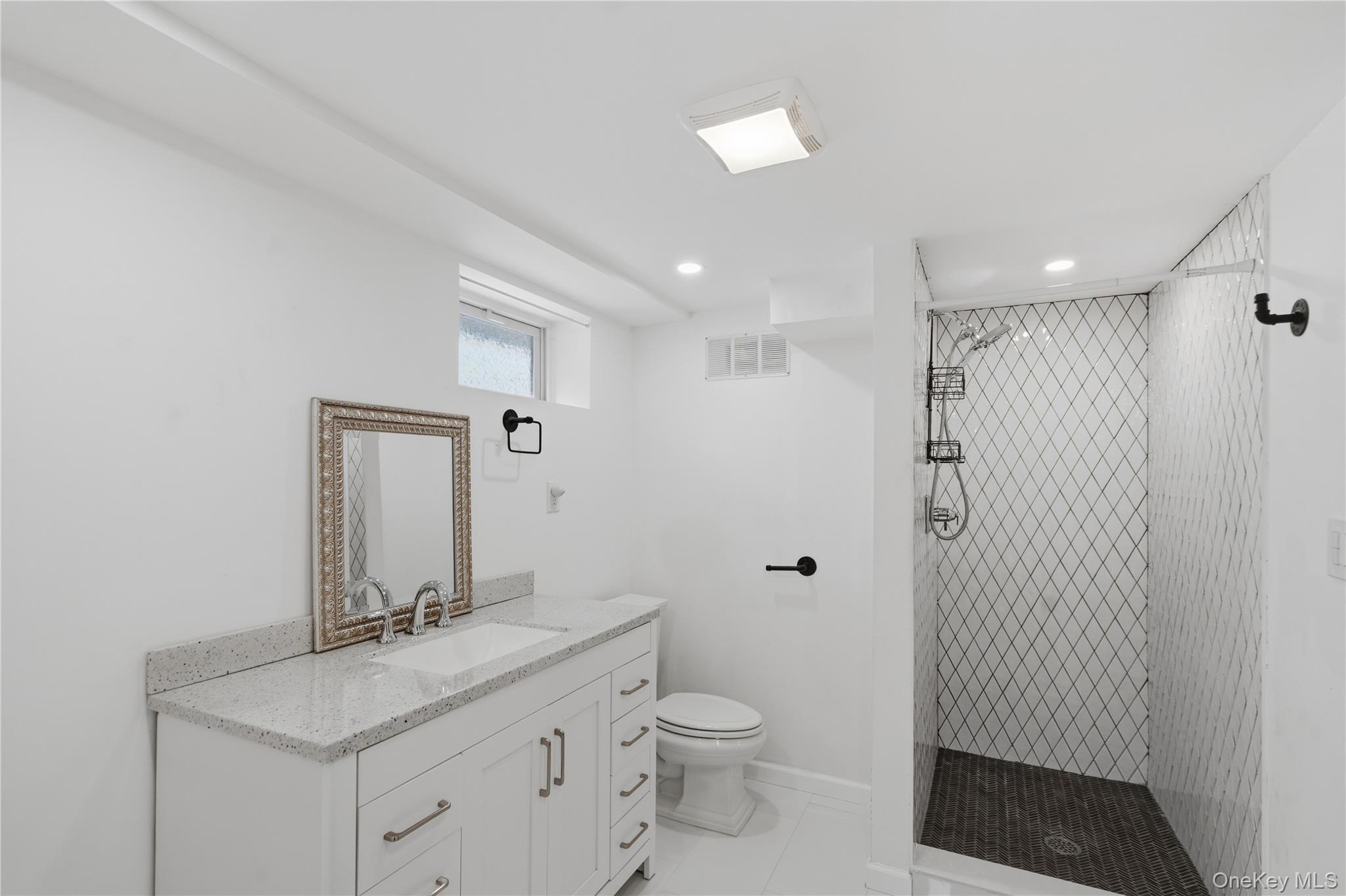 Bathroom with a white vanity and a spacious walk-in shower tiled in a dark diamond pattern.