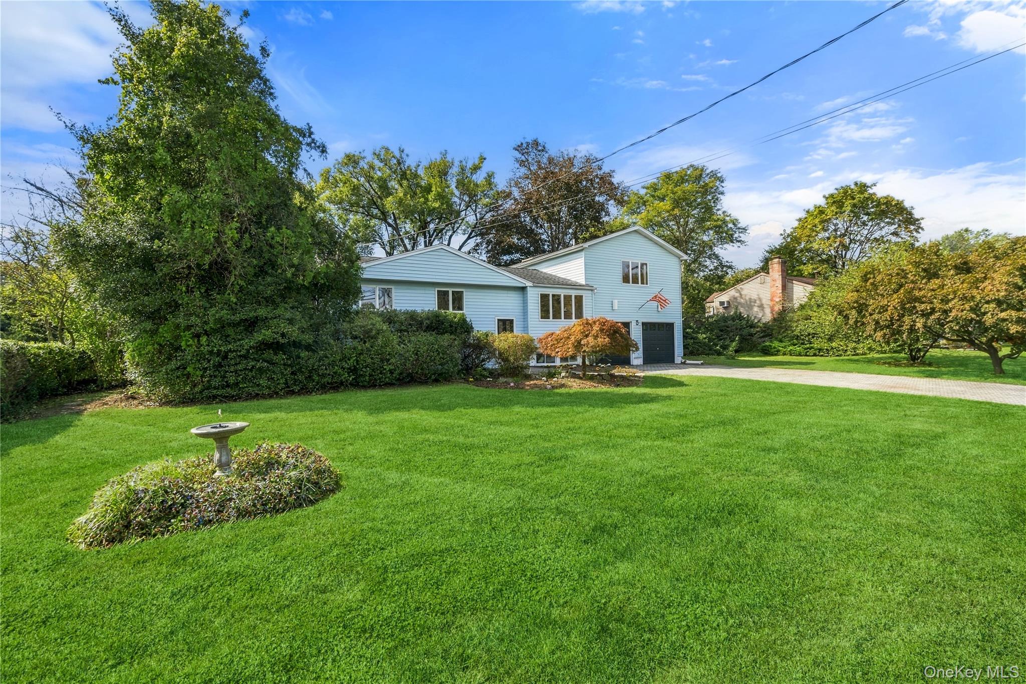 Light blue split-level home behind a broad lawn, with a birdbath and paved driveway.