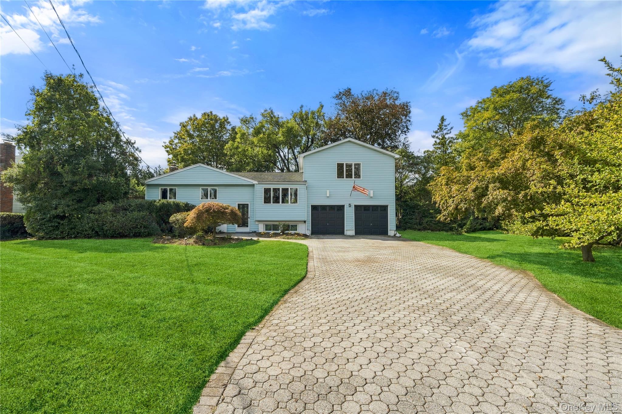 Light-blue two-story home with a two-car garage, paver driveway, and spacious green lawn.