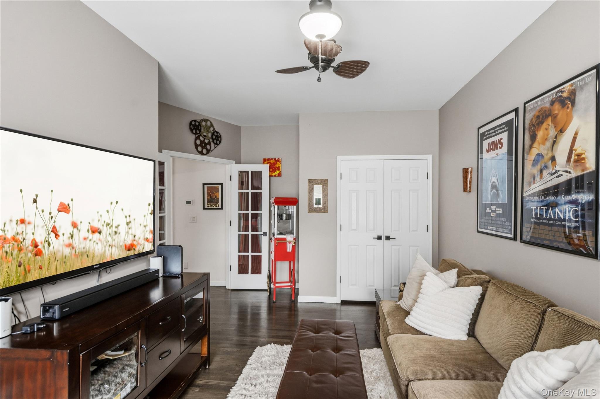 Furnished living room with a beige sectional, large television, red popcorn machine, and framed movie posters.