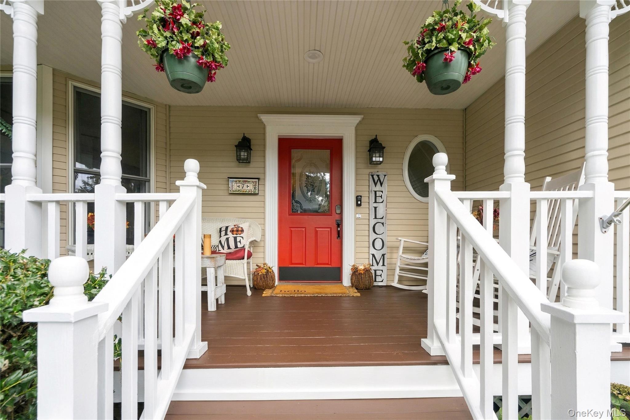 Covered front porch with white railings, hanging flowers, and a bright red front door.