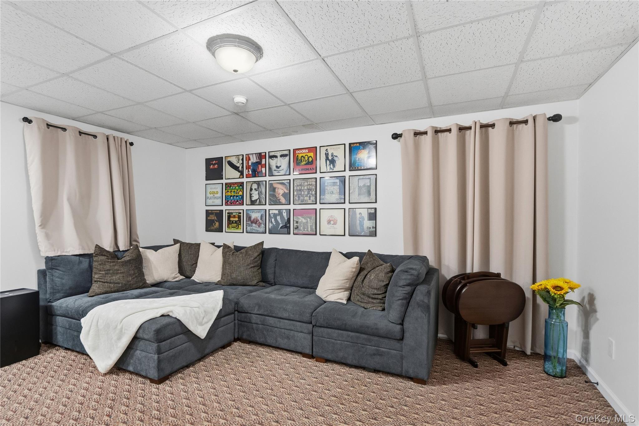 Lounge with a charcoal sectional, framed album artwork, beige curtains, and patterned carpet.