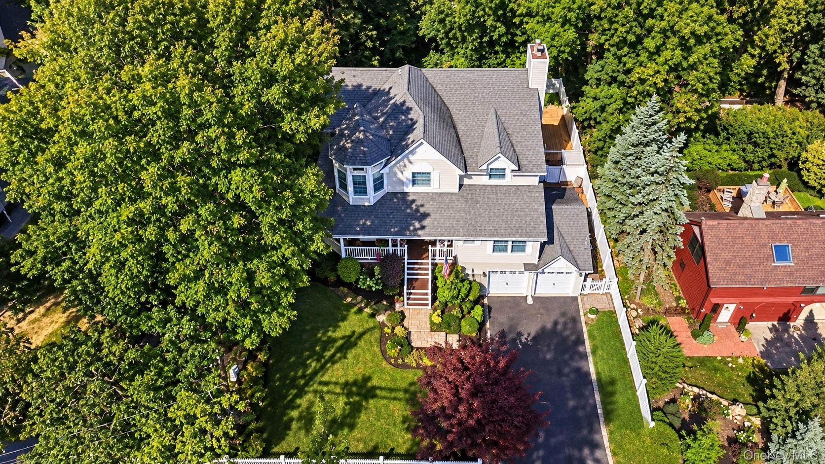 Aerial view of a two-story home with a double garage, long driveway, and mature trees.