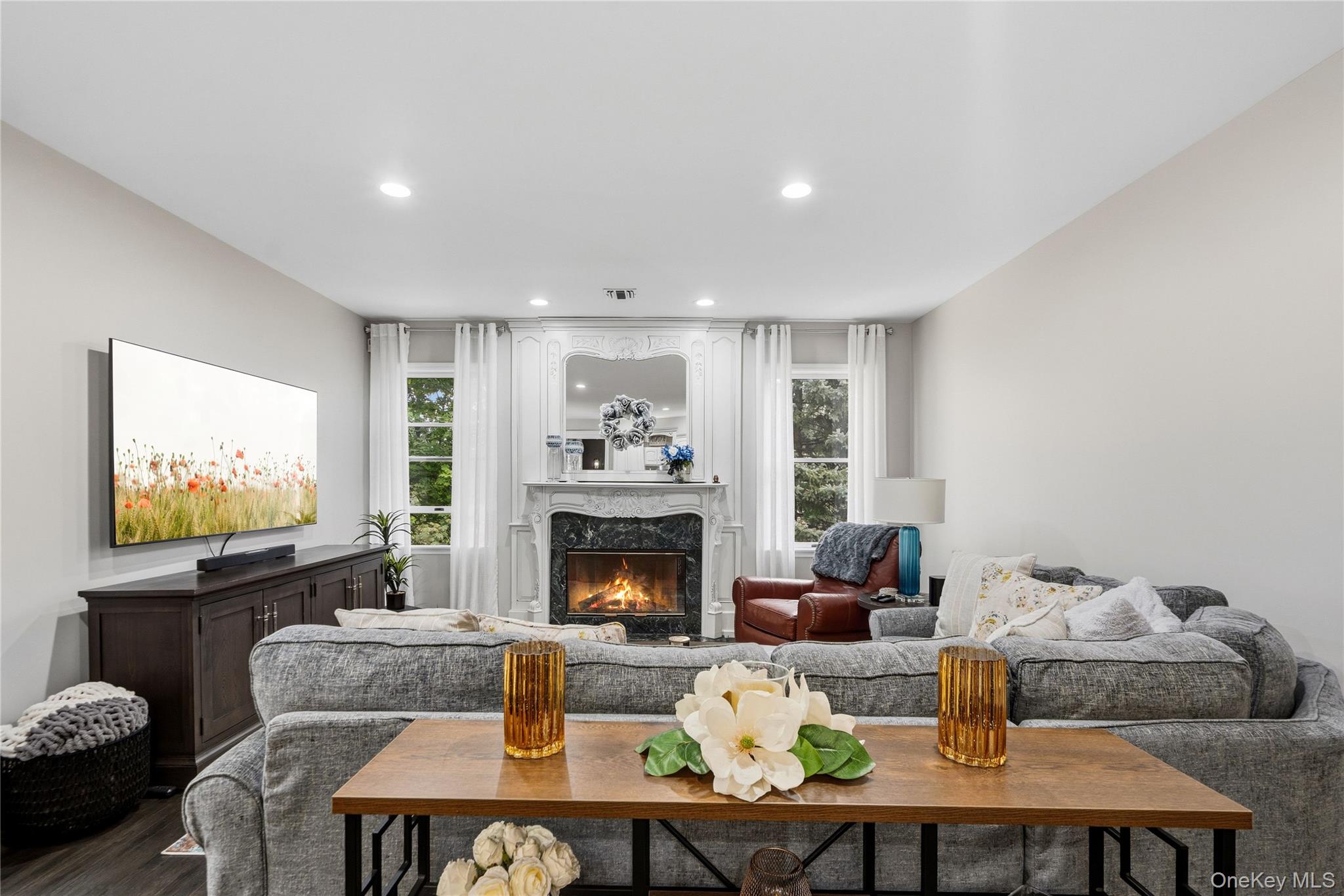 Living room with a gray sectional, ornate white fireplace, and tall curtained windows.