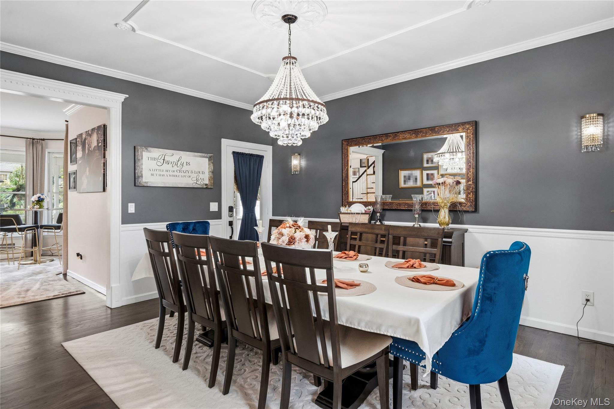 Dining room with a crystal chandelier, long table, dark wood chairs, and blue velvet accent chairs.