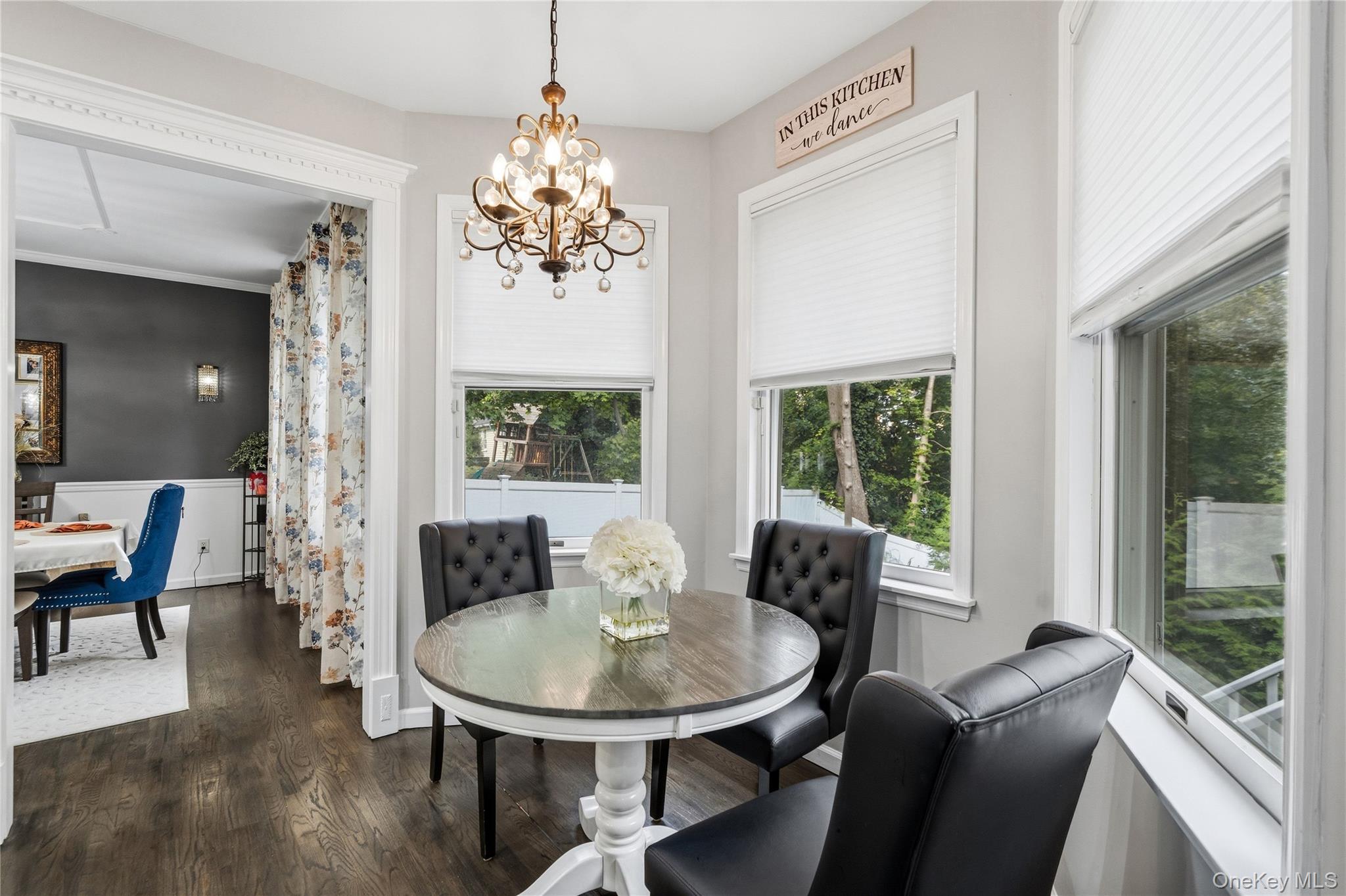 Dining nook with a round table, black leather chairs, chandelier, and large windows overlooking trees.