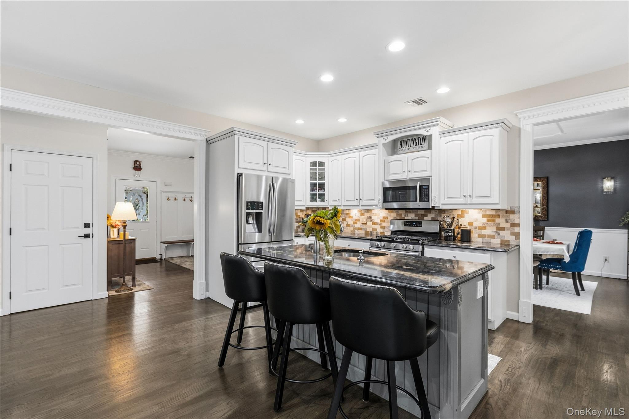 Kitchen with white cabinets, stainless steel appliances, and a large stone island with black bar stools.