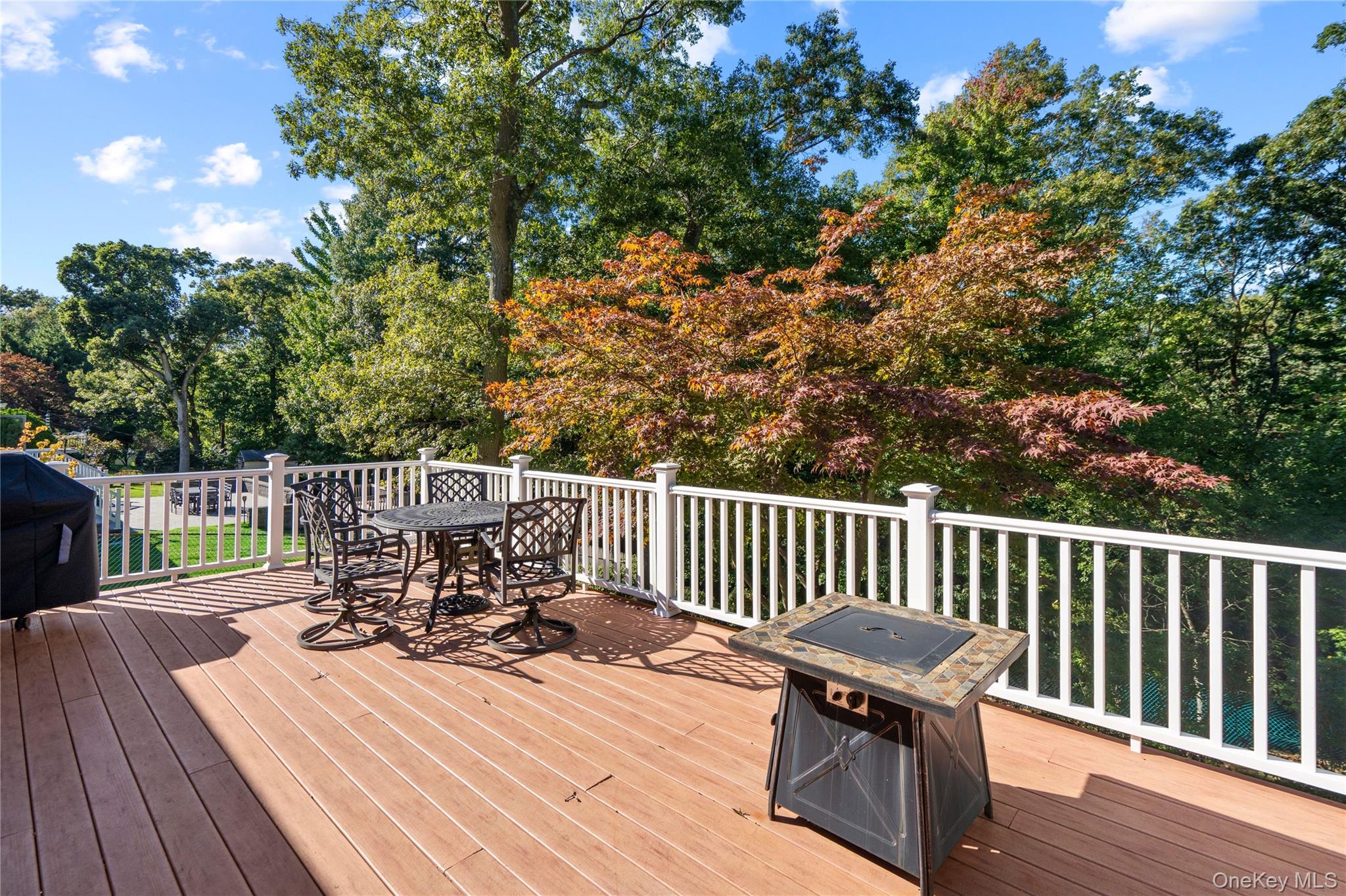 Wooden deck with patio dining set and grill overlooking leafy trees.