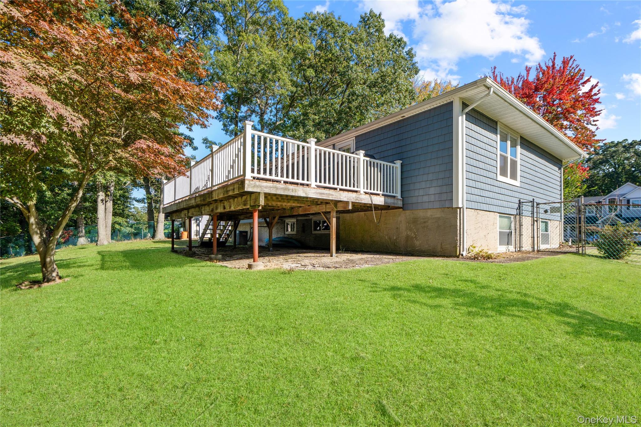 Rear of a blue-gray house with a raised white-railed deck overlooking a broad lawn.