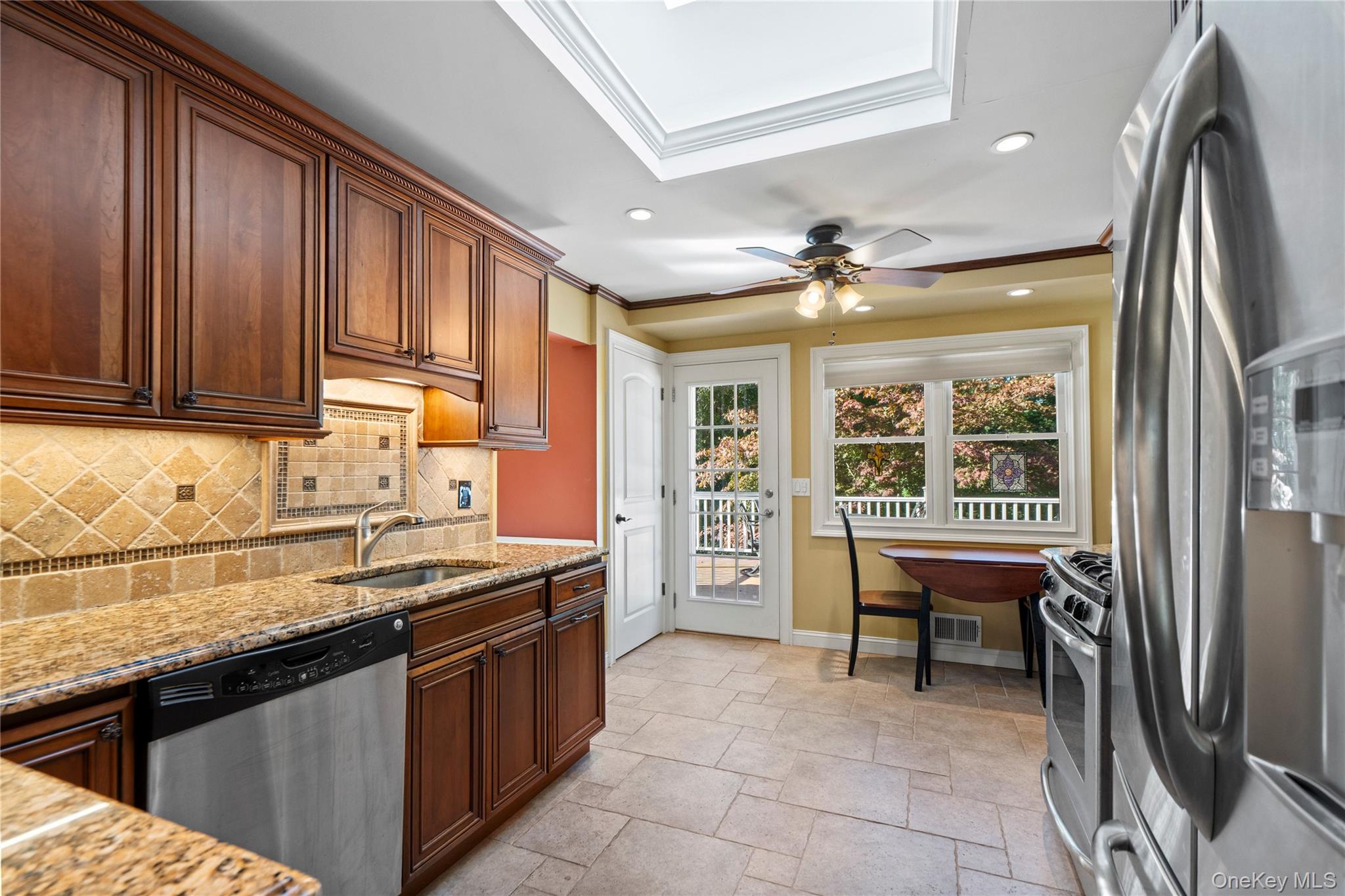 Kitchen with dark wood cabinets, granite counters, stainless steel appliances, and a skylight.