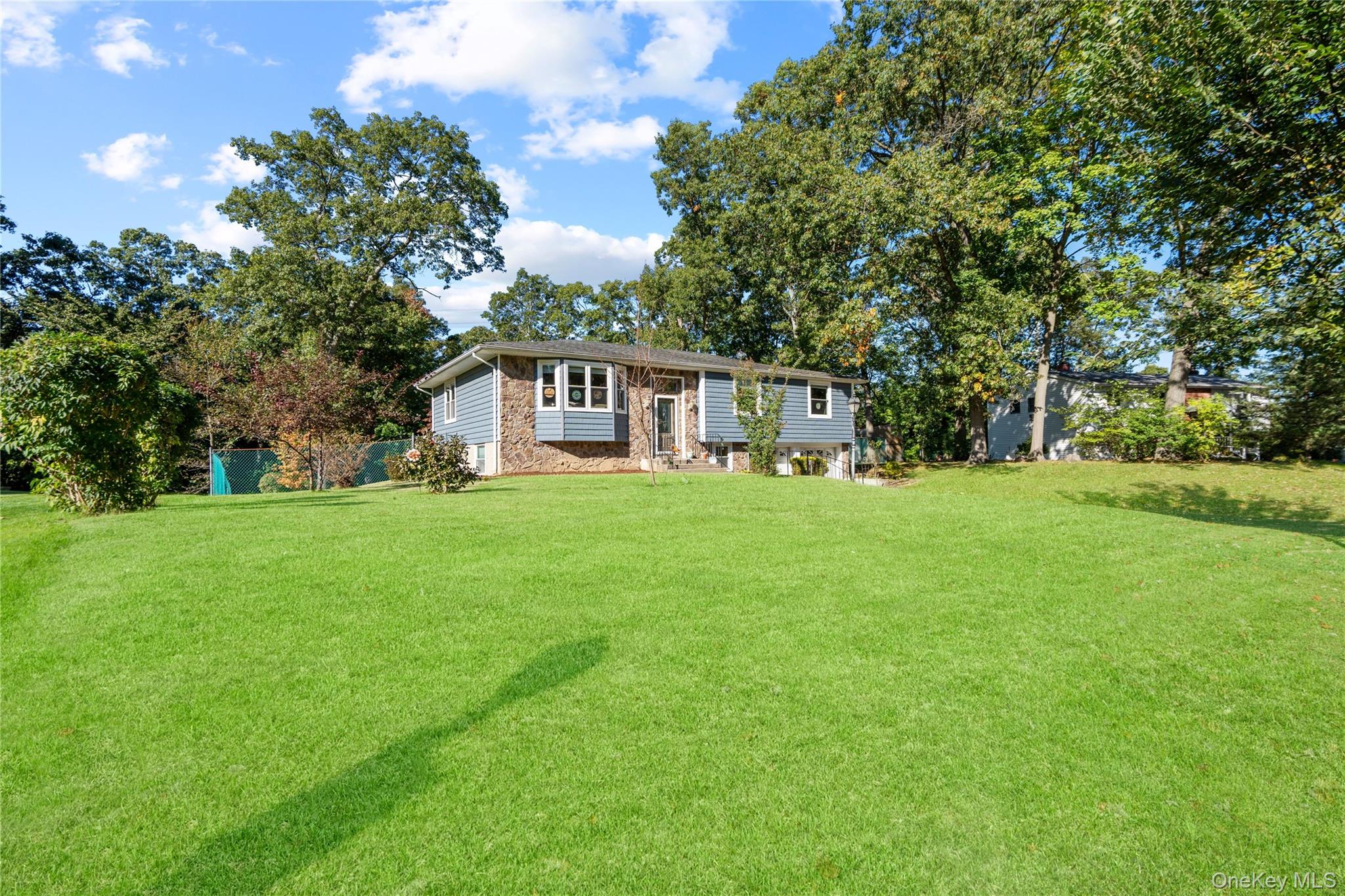 Raised ranch with blue siding and stone accents behind a broad lawn and mature trees.