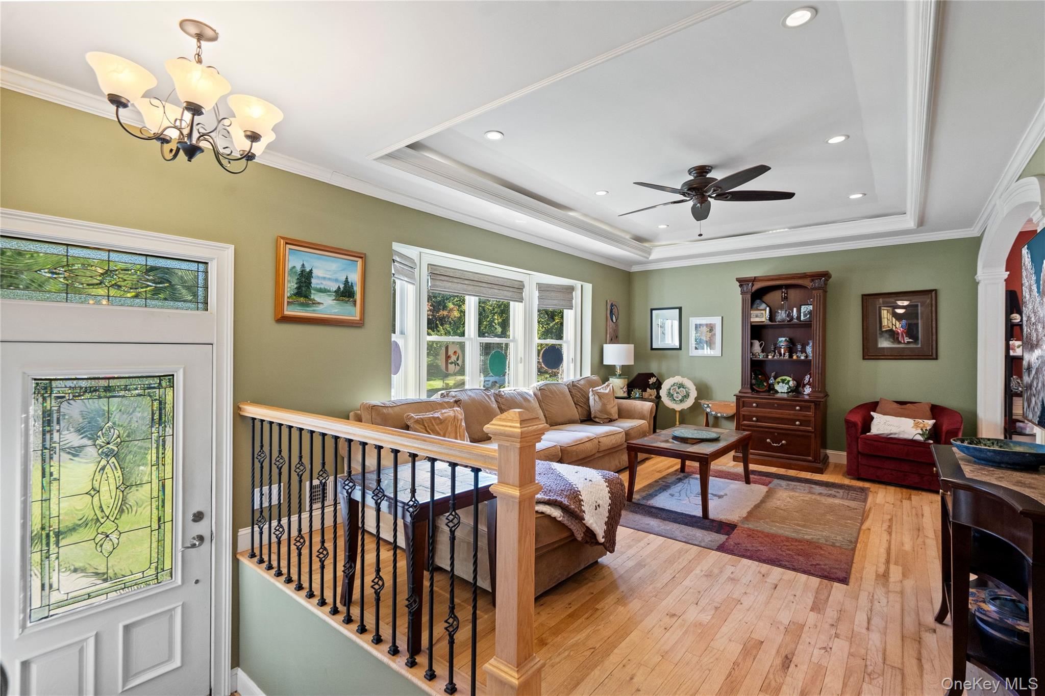 Living room with tan sectional, hardwood floors, tray ceiling, stained-glass front door, and sage-green walls.
