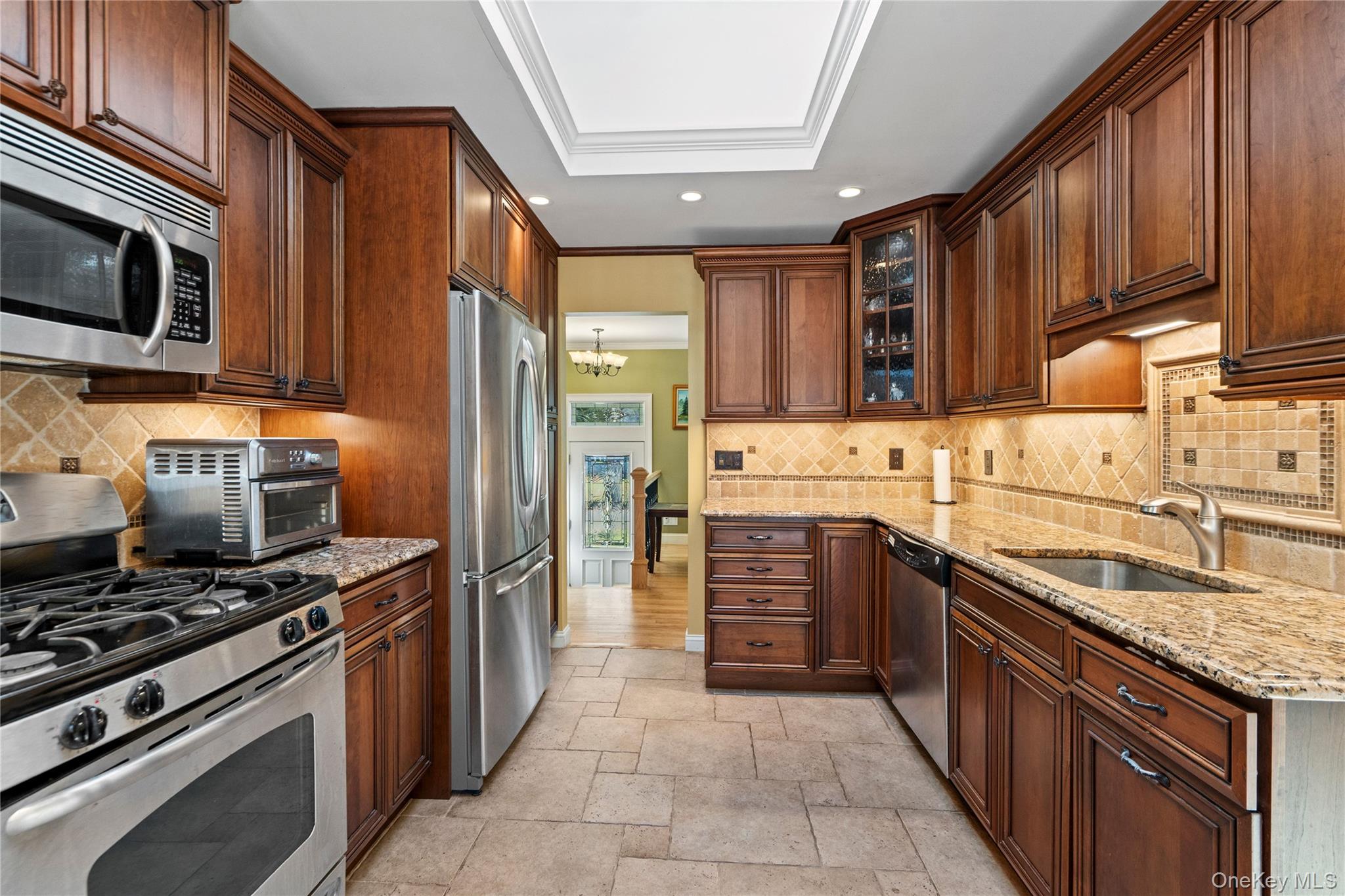 Galley kitchen with cherry cabinets, granite counters, stainless steel appliances and a tiled backsplash.