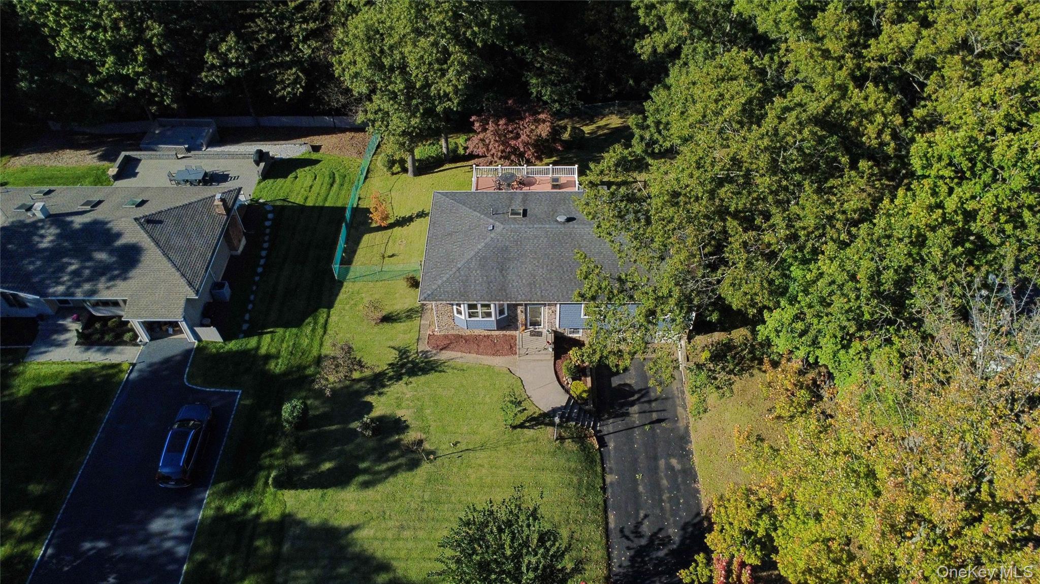 Aerial view of a home with a broad lawn, mature trees, and a raised rear patio.
