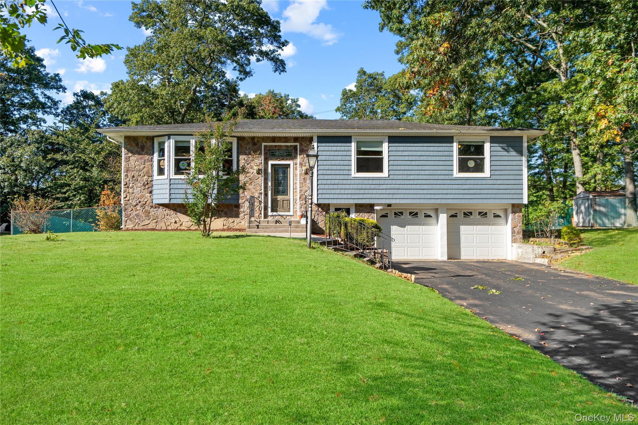 Split-level home with blue siding, stone facade, two-car garage, and broad front lawn.