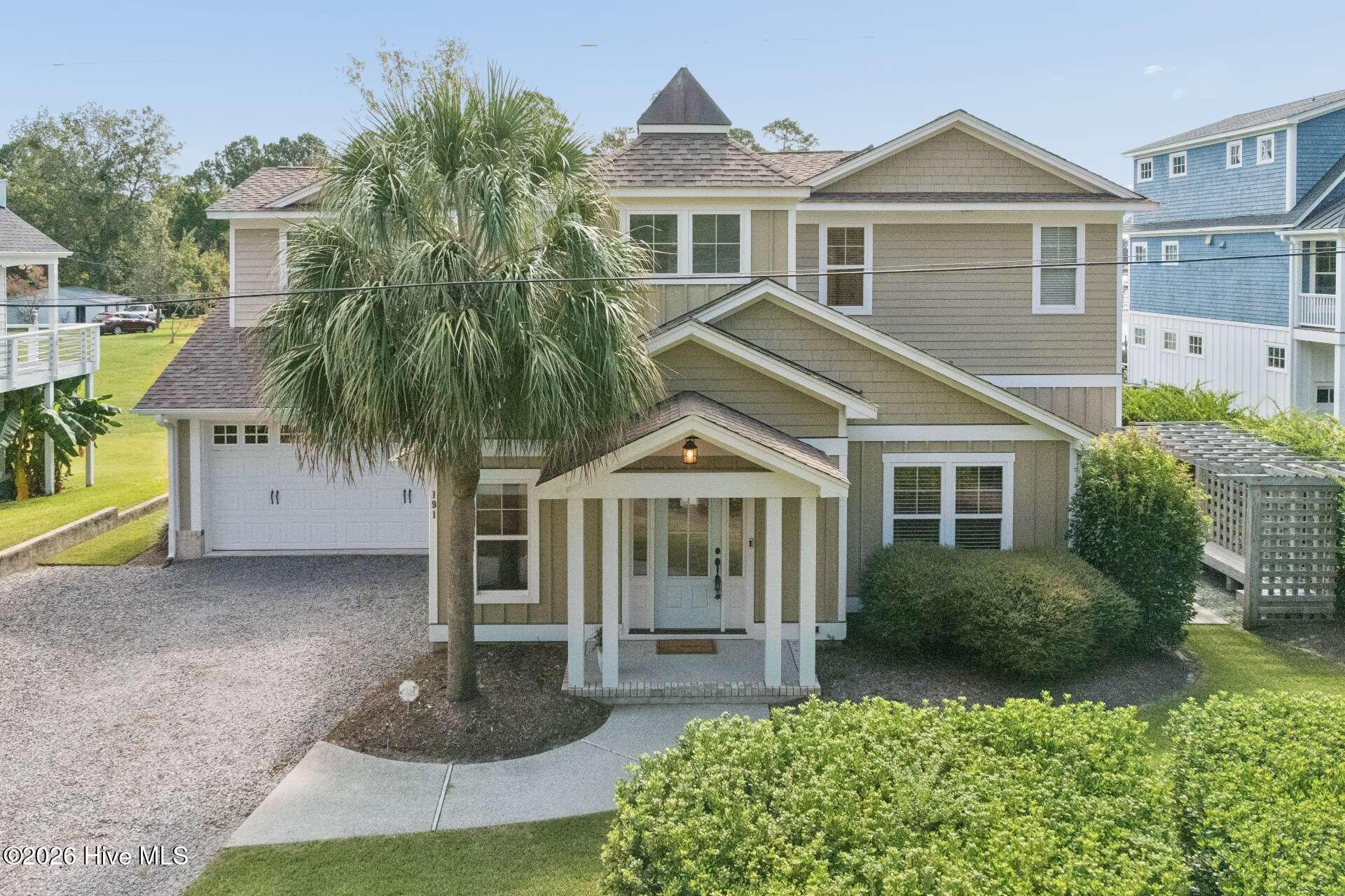 Two-story tan home with a covered porch, attached garage, and large palm tree in front.