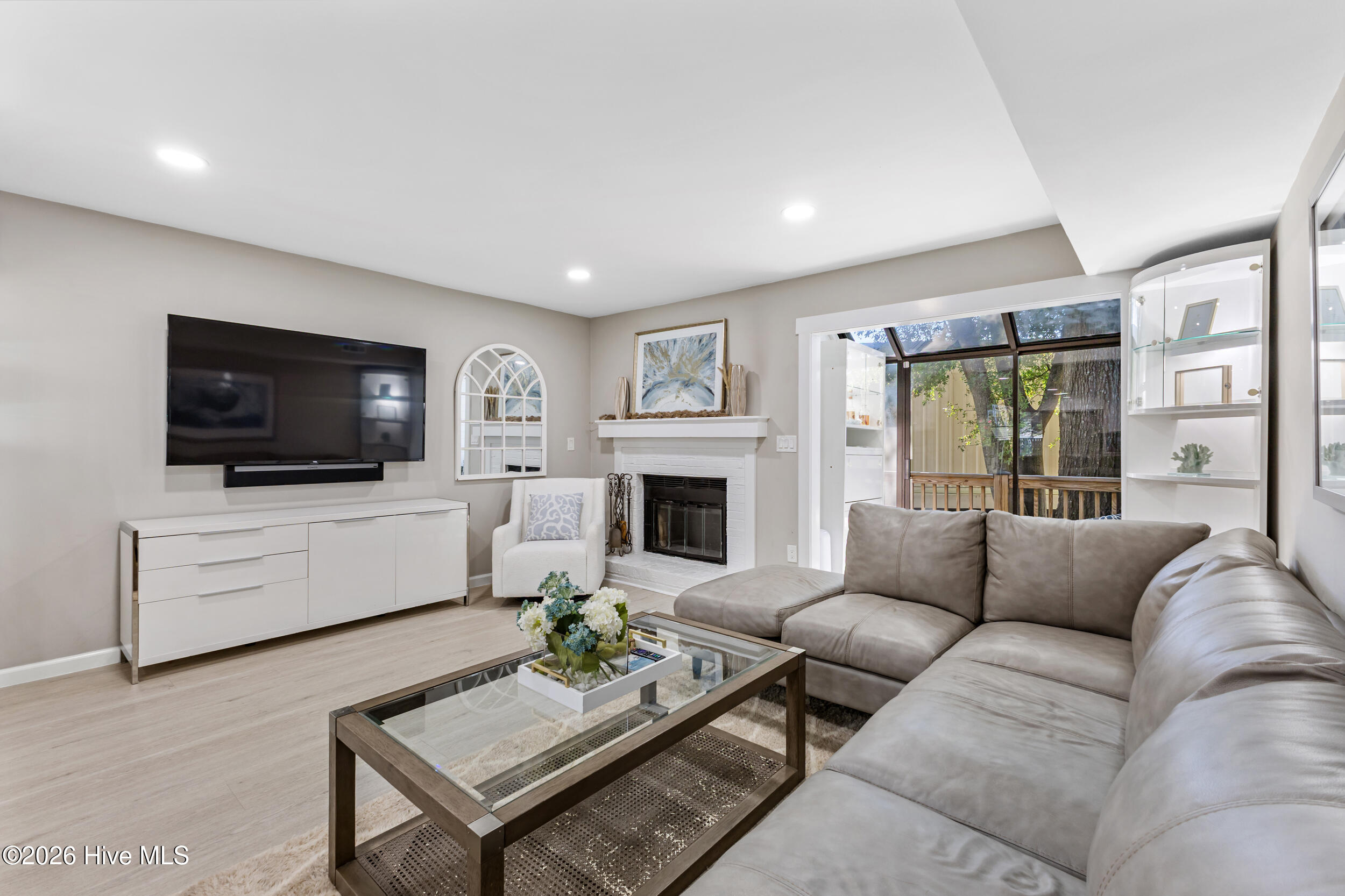 Living room with a large sectional, white fireplace, wall-mounted TV, and glass doors to a deck.