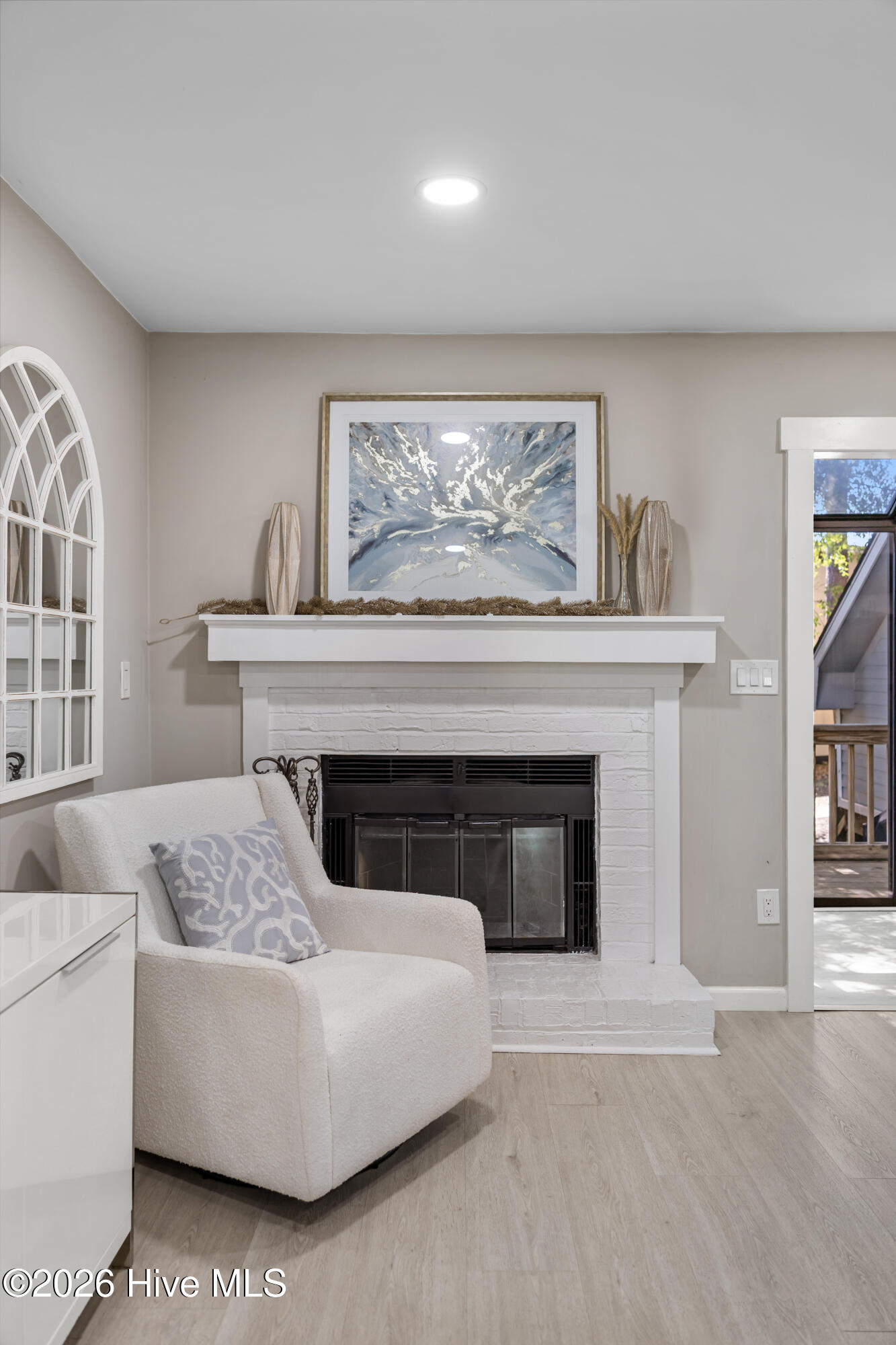 Living room with a white brick fireplace, black firebox, and white armchair beside a deck door.