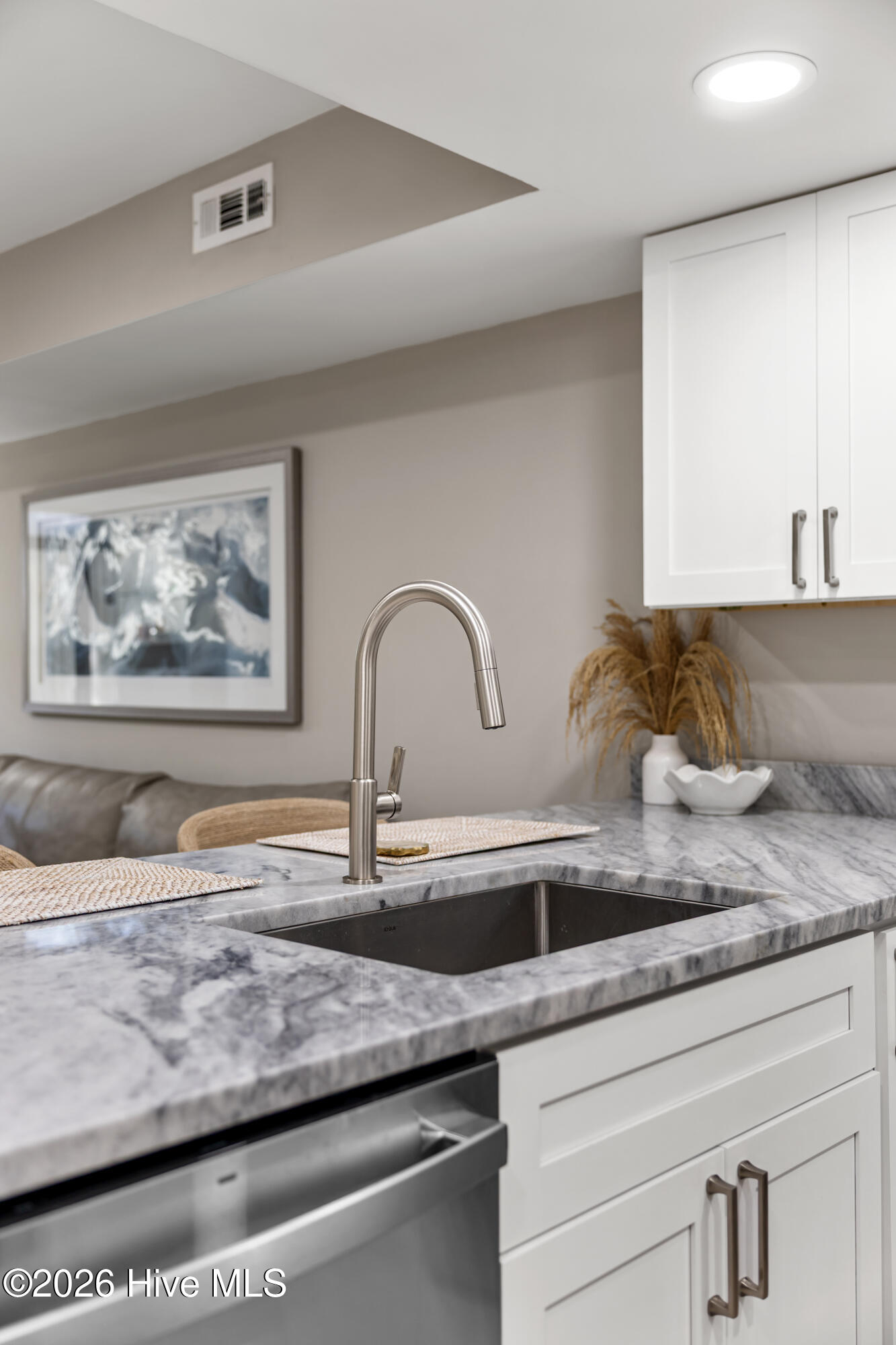 Kitchen sink with a tall stainless faucet, veined marble countertop, and white cabinetry.