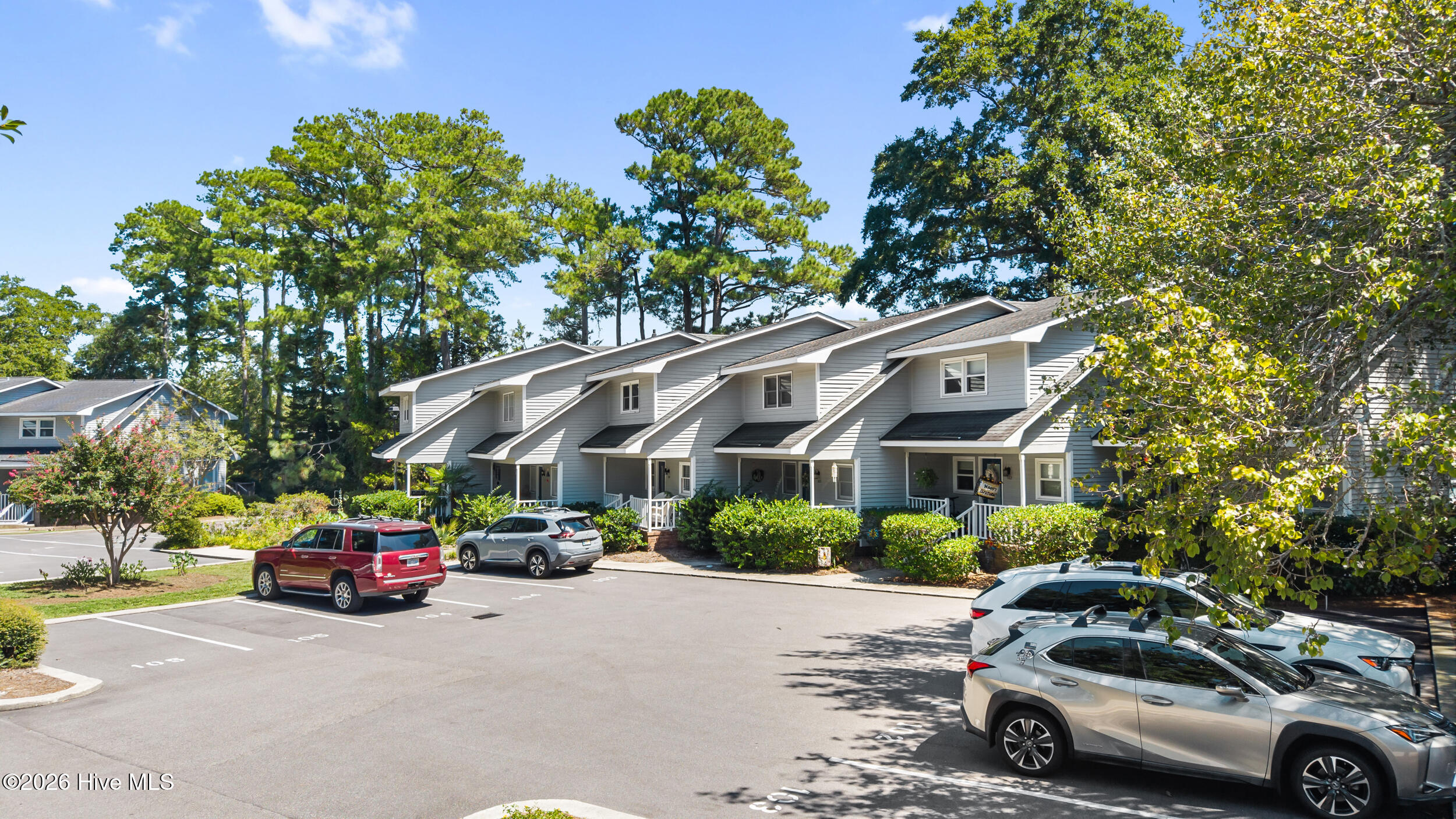 Gray-sided attached homes with covered porches, mature trees, and a shared parking lot.