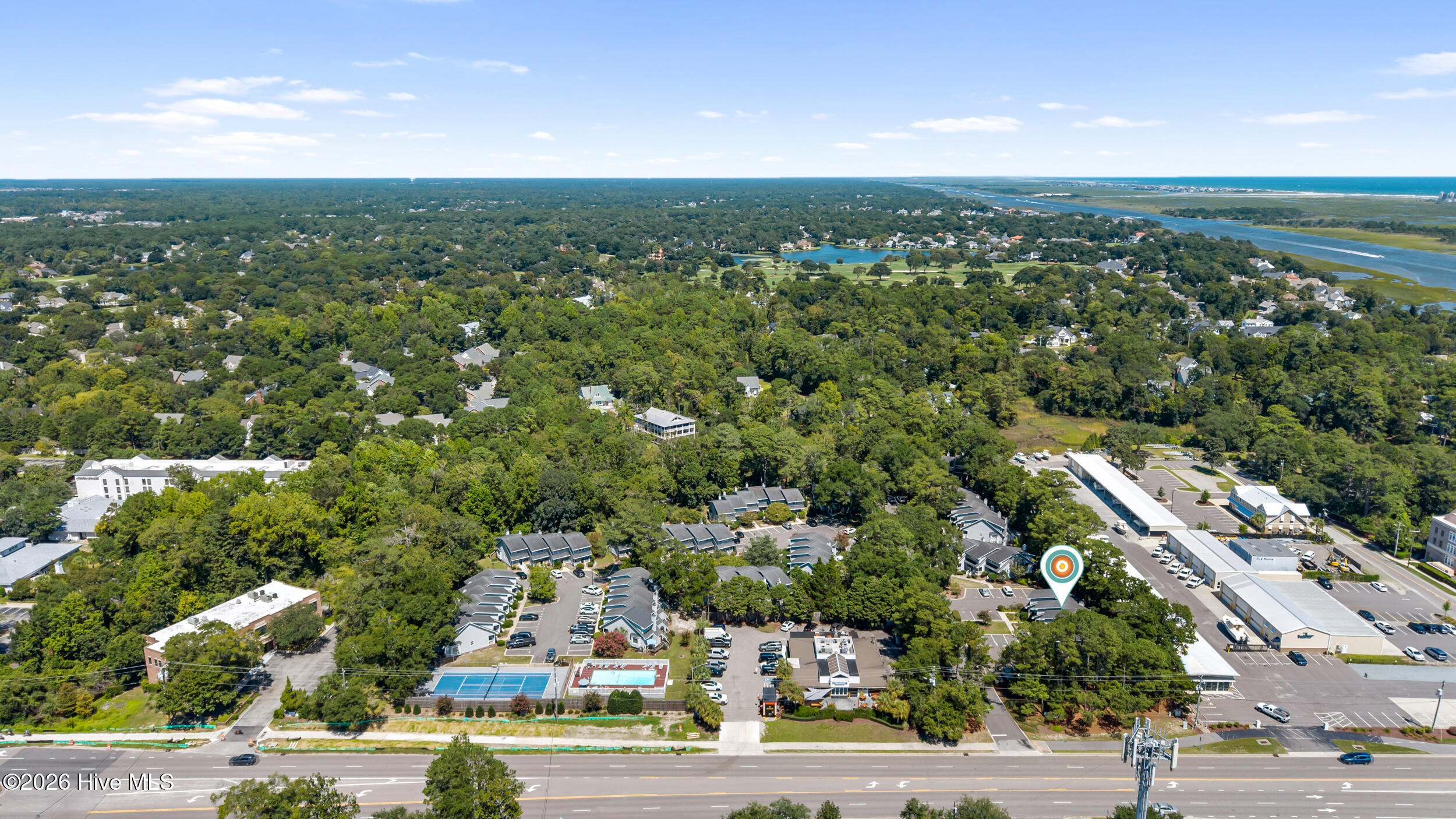 Aerial view of the property area, with wooded neighborhoods, tennis courts, pools, and coastal waterways.
