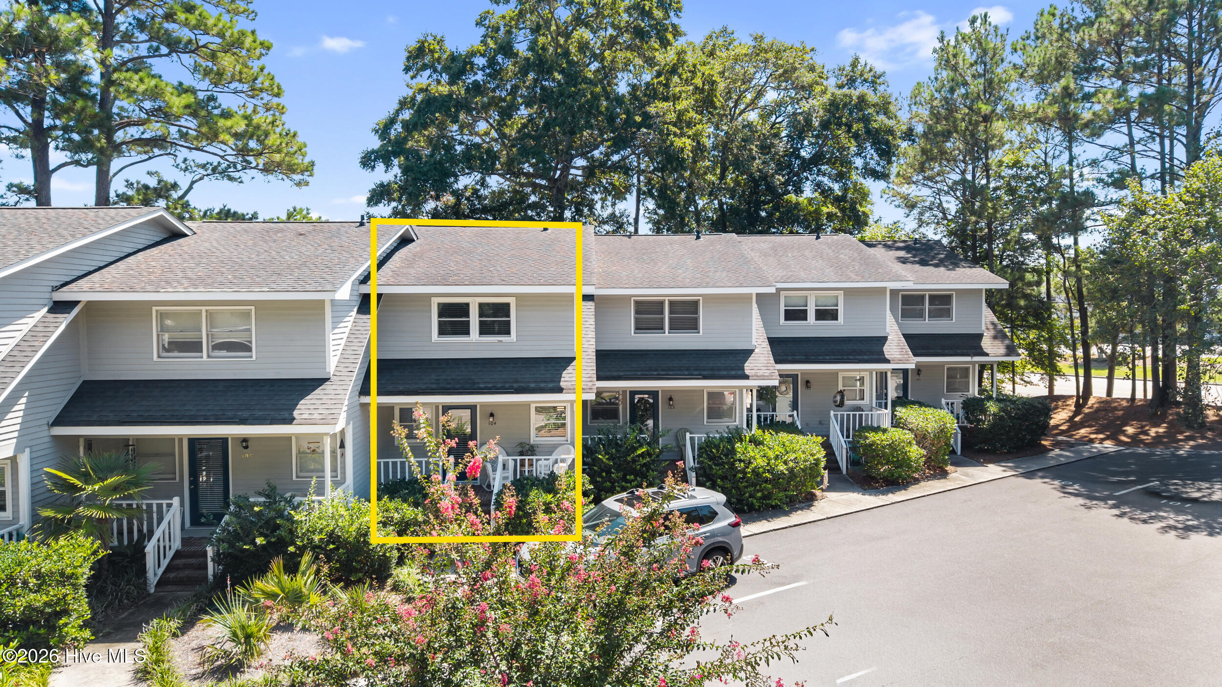 Gray townhome outlined in yellow, with a covered porch and flowering shrubs.