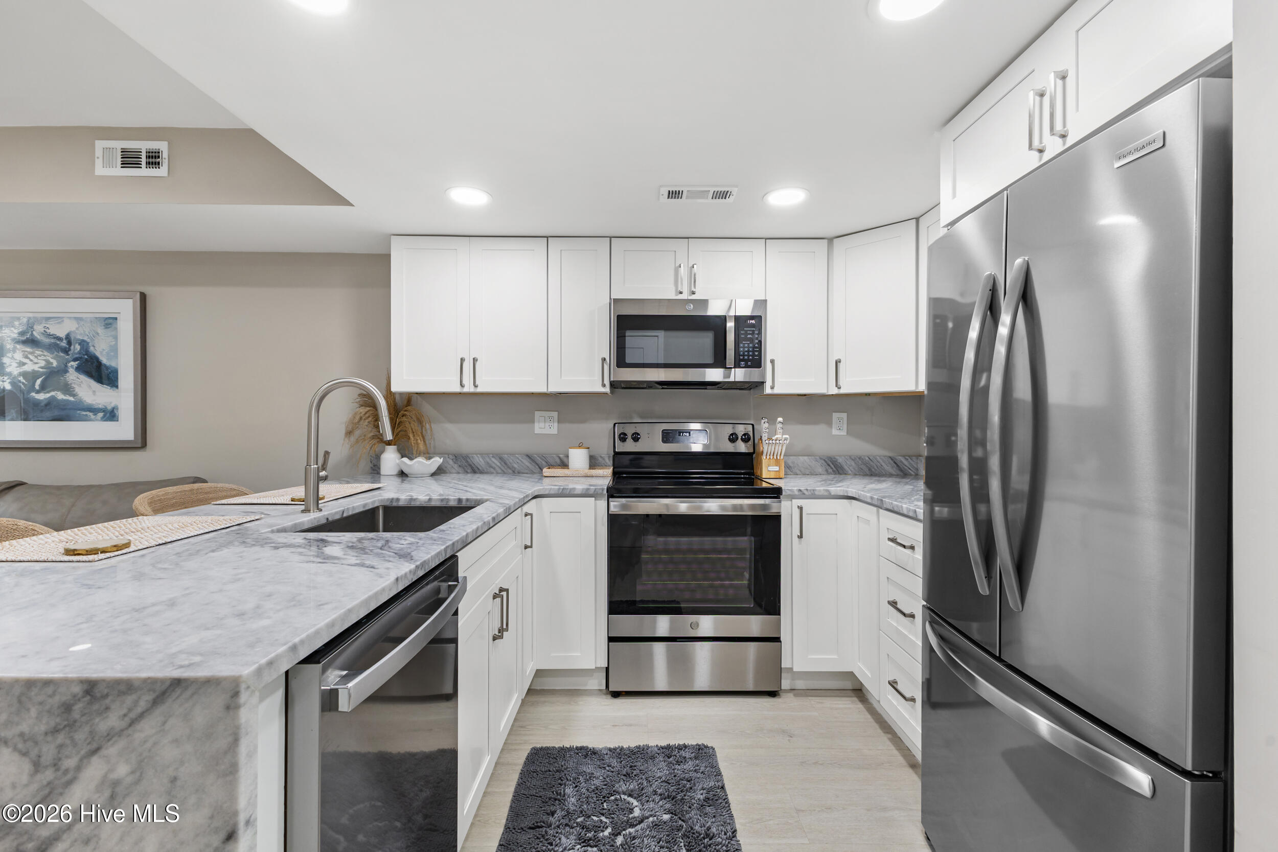 Bright kitchen with white cabinets, gray marble-look counters, and stainless steel appliances.