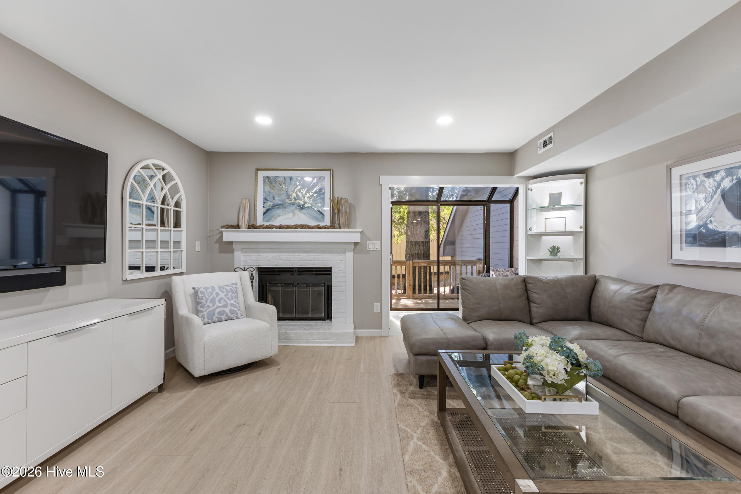 Living room with a white brick fireplace and gray sectional beside sliding glass doors to a deck.