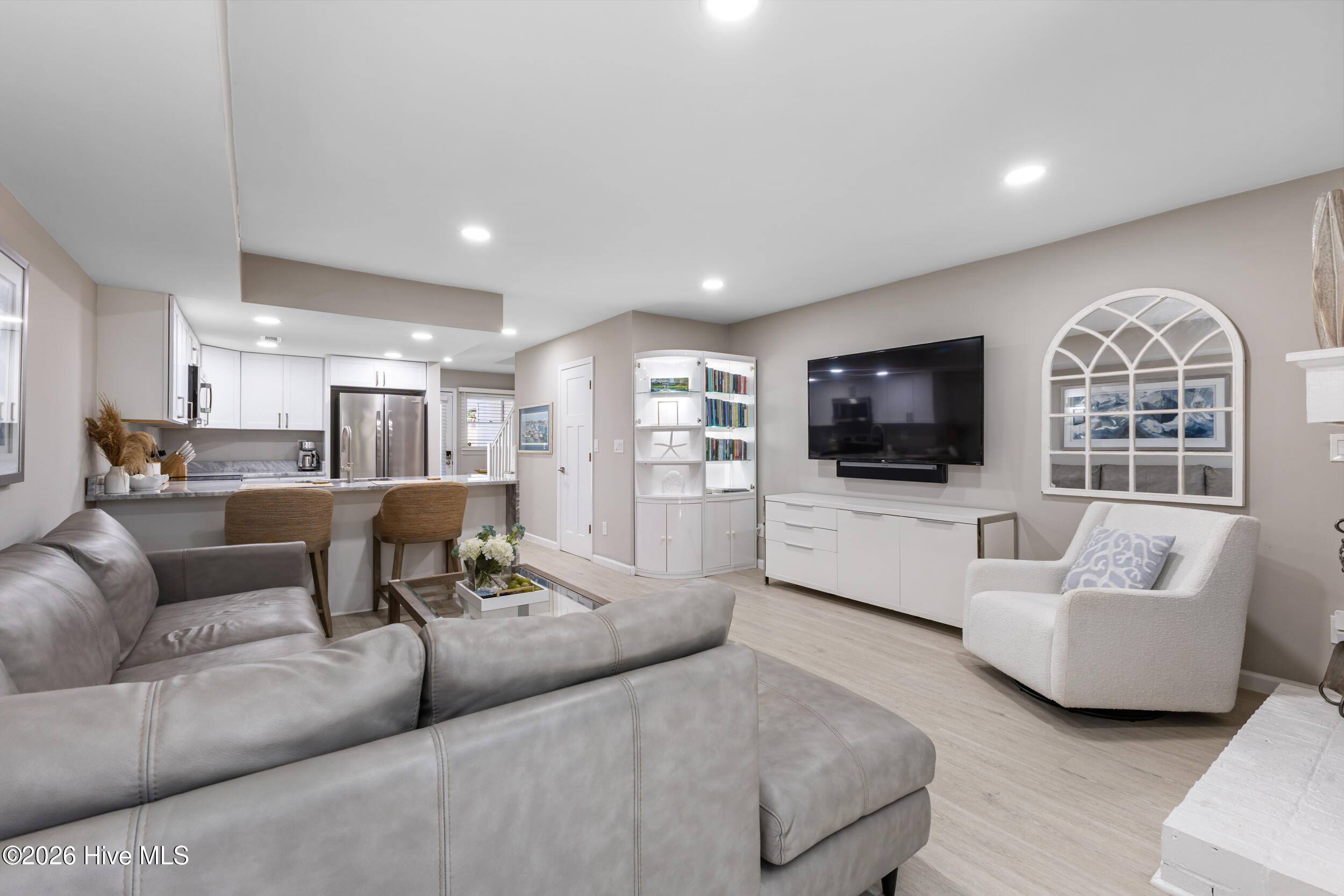 Open-plan living room and kitchen with a gray sectional, breakfast bar, and wall-mounted television.
