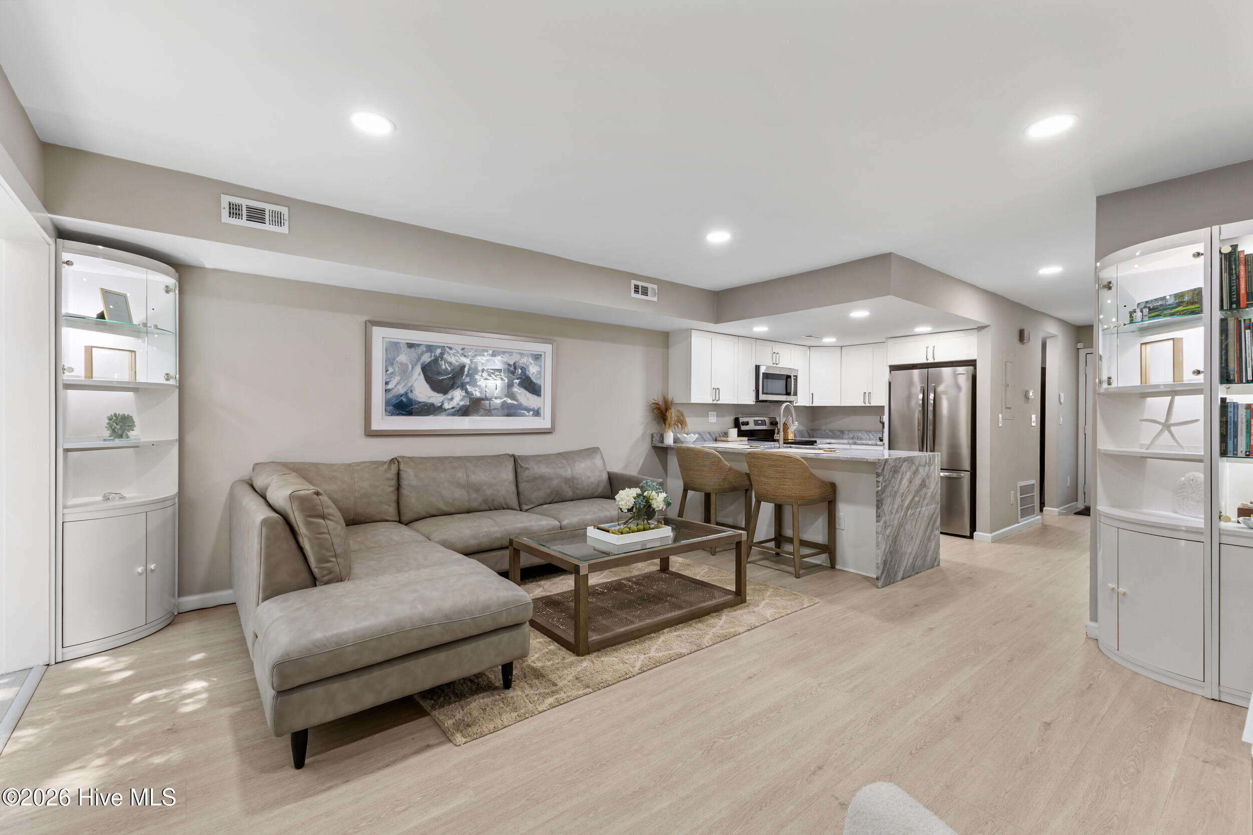 Open-plan living room and kitchen with a gray sectional, white cabinetry, and marble-look island.